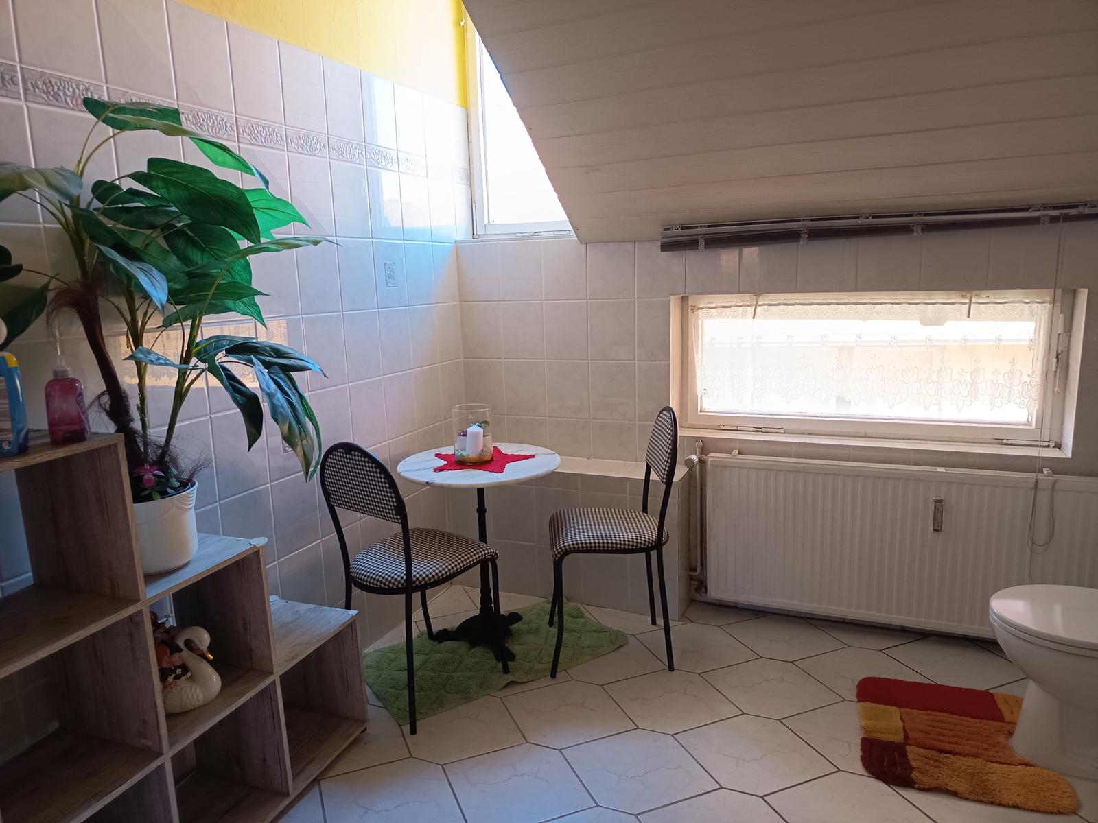 Badezimmer mit Tisch, zwei Stühlen, Pflanze und Fenster.