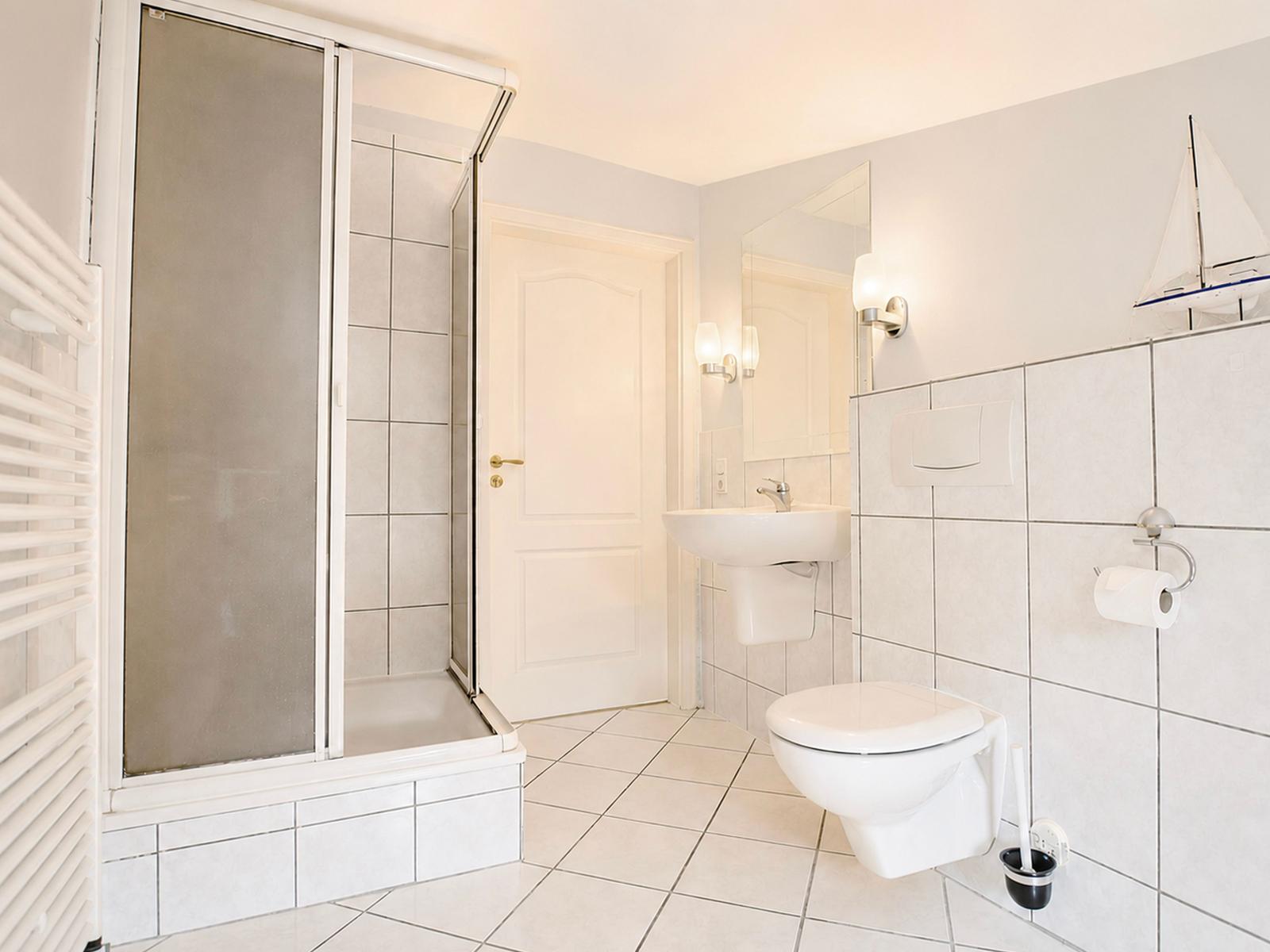 Bad mit Dusche, Waschbecken und Toilette. Wandtisch mit Segelbootmodell.