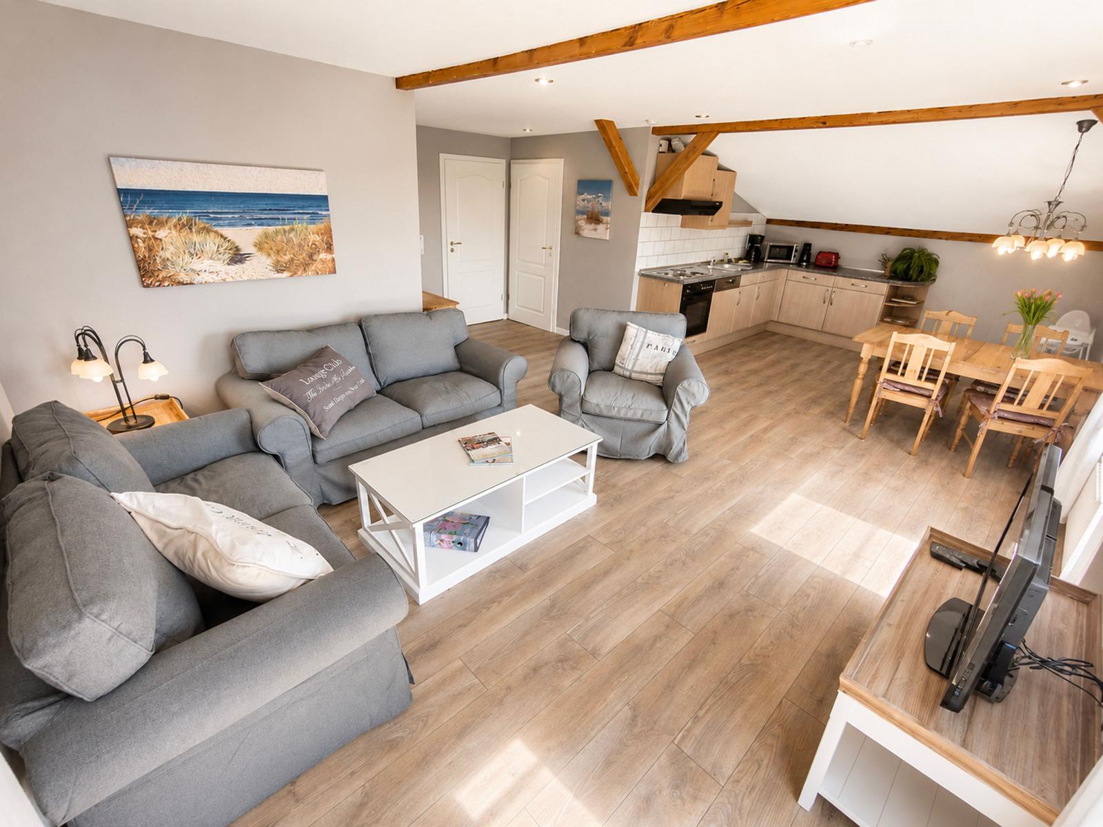 Wohnzimmer mit Sofa, Couchtisch und Küchenbereich. Holzboden und Balken.