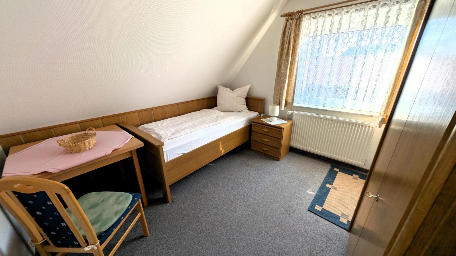 Ein Schlafzimmer mit Einzelbett, Schreibtisch und Fenster mit Vorhängen.
