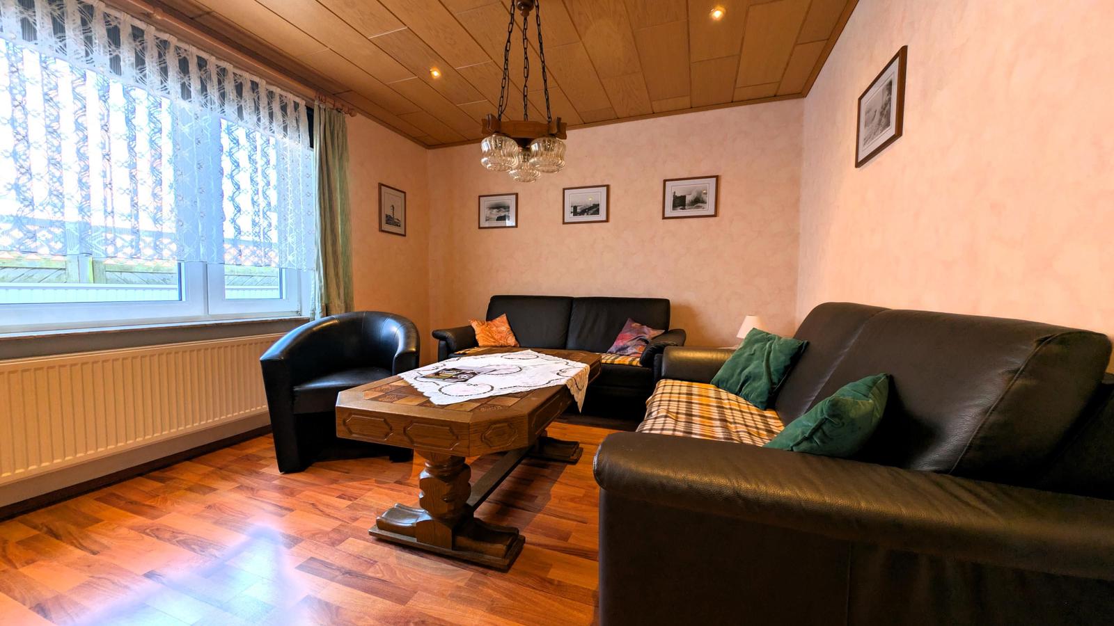 Wohnzimmer mit zwei Sofas, einem Sessel und einem Holztisch. Holzfußboden und Holzdecke.