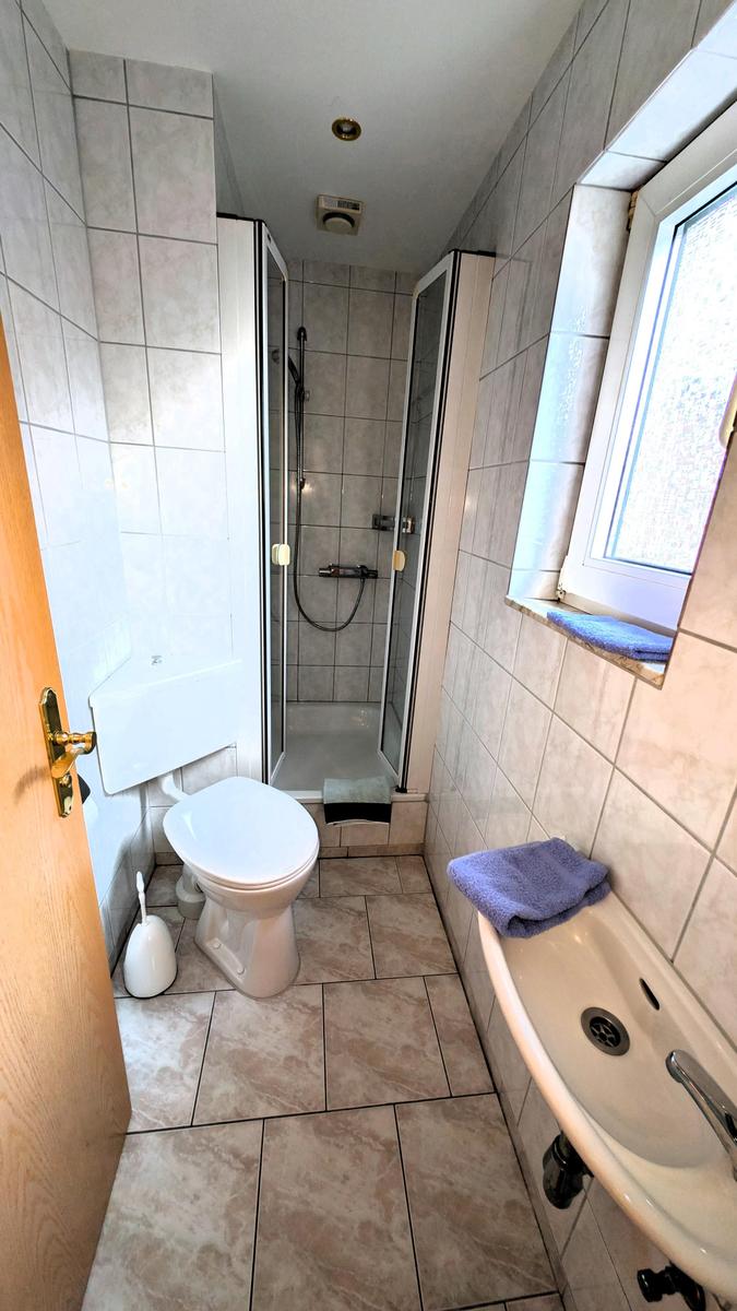 Badezimmer mit Dusche, Toilette und Waschbecken. Fenster mit Handtuch.