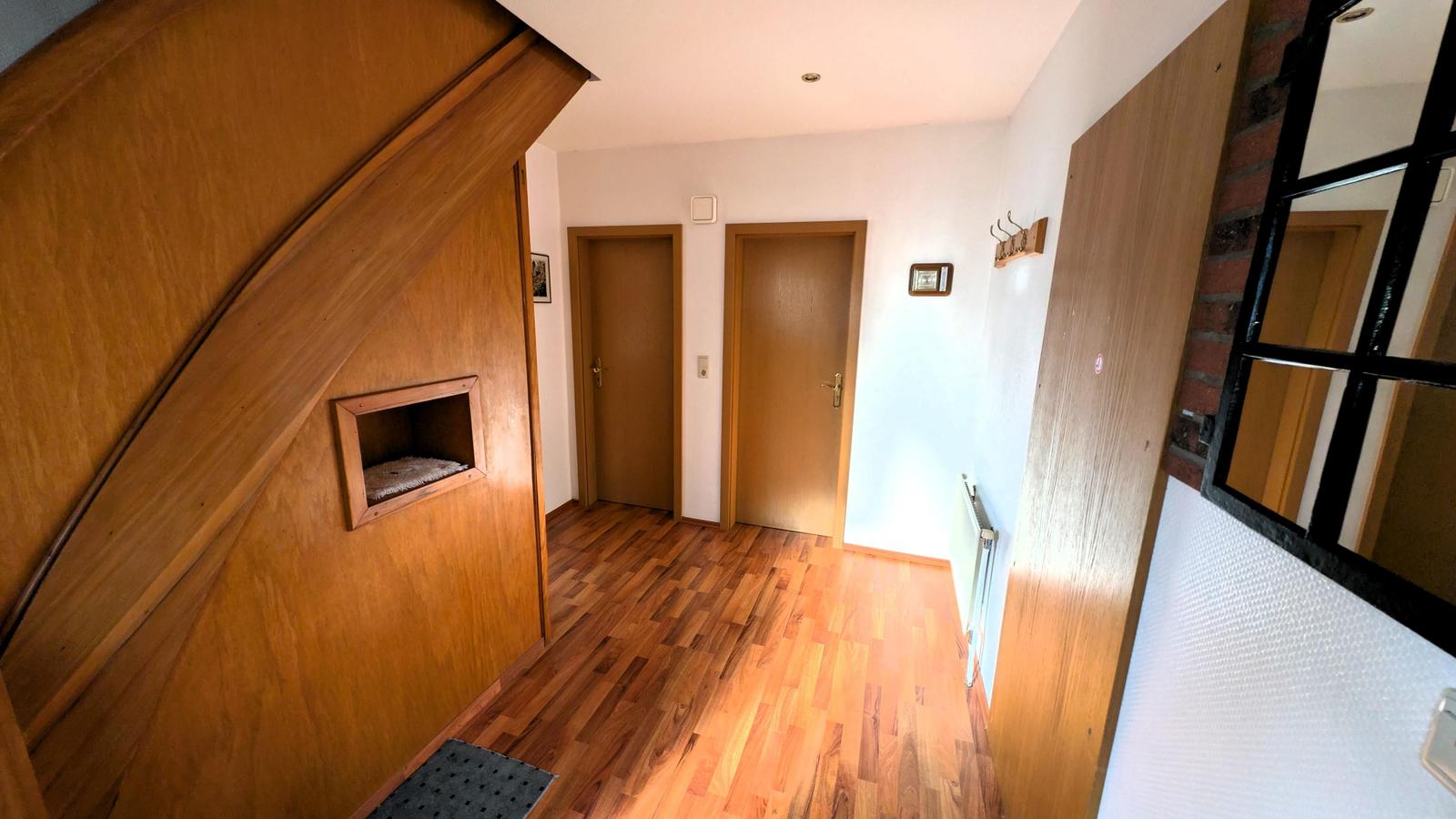 Flur mit Holzboden, zwei Türen und Holzwand mit eingelassener Nische.