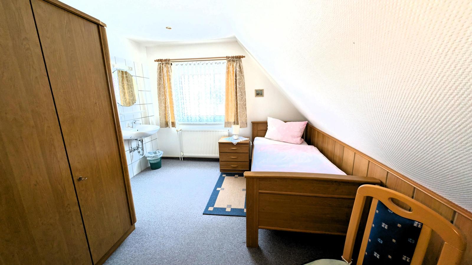 Ein Schlafzimmer mit Bett, Kleiderschrank und Bad. Dachneigung und Fenster sichtbar.