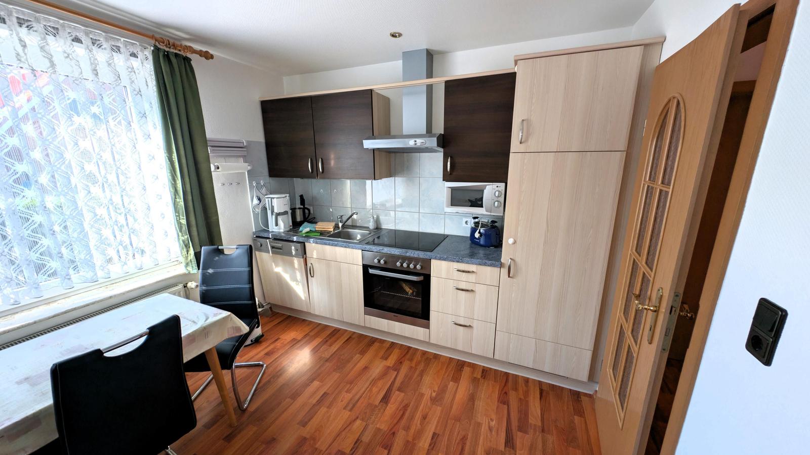 Küche mit Essbereich, Holzboden und Fenster mit Vorhängen.