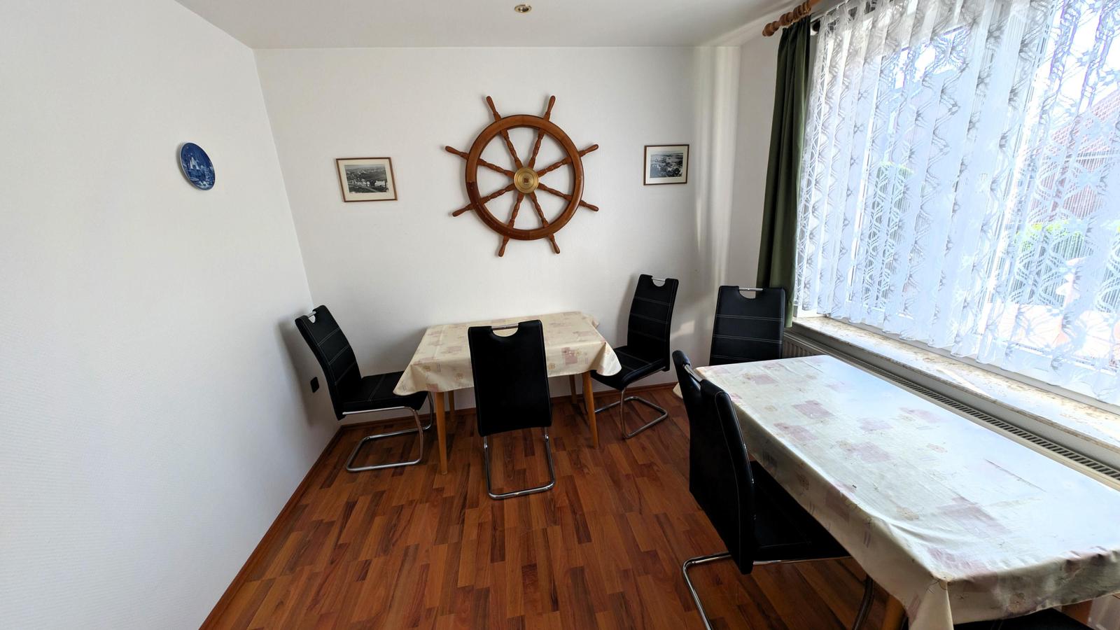 Esszimmer mit zwei Tischen, schwarzen Stühlen und hölzernem Boden. Wanddekoration mit Ruder und Bildern.