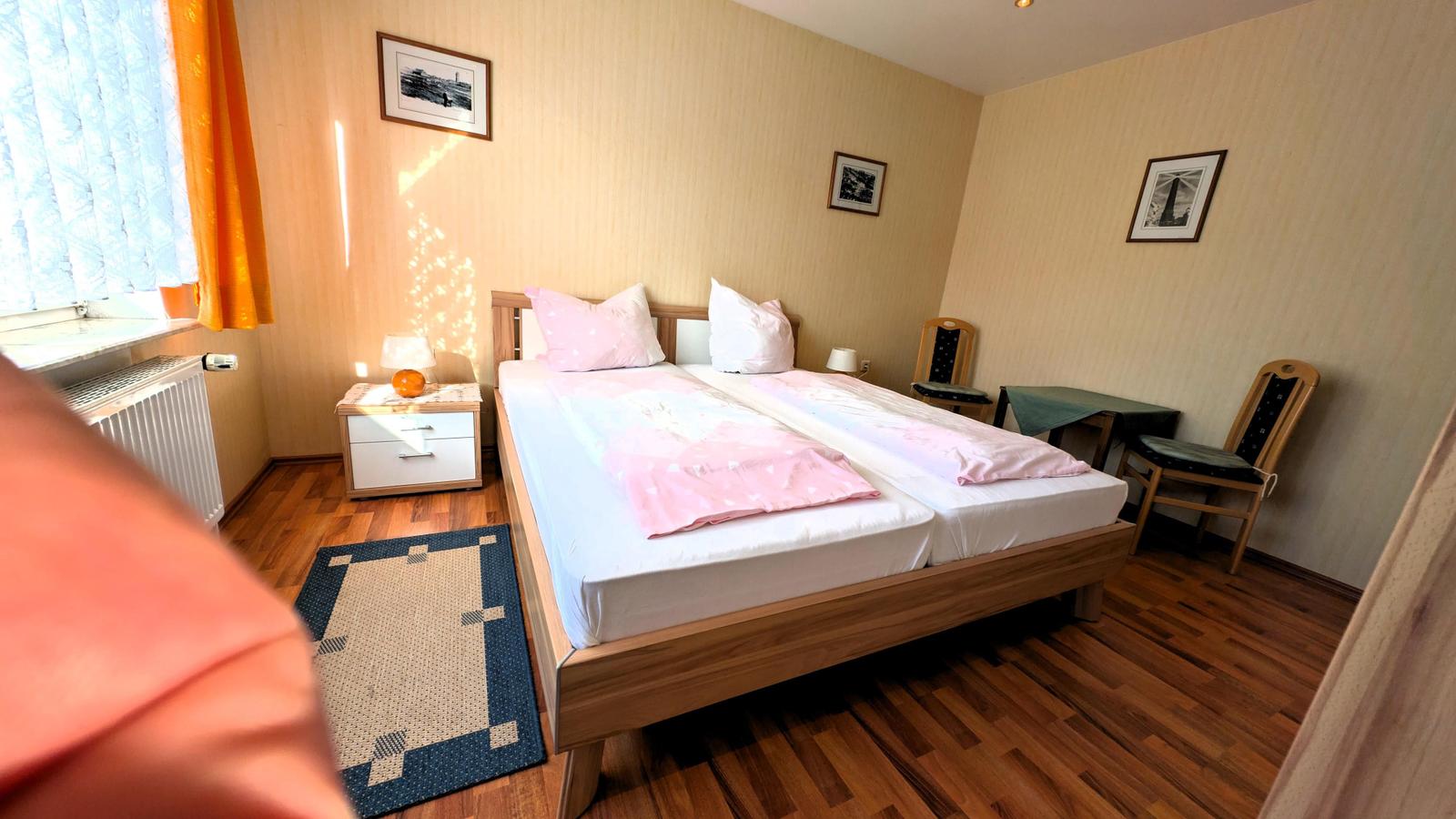 Schlafzimmer mit Doppelbett, Holzboden und Fenster mit Vorhängen.