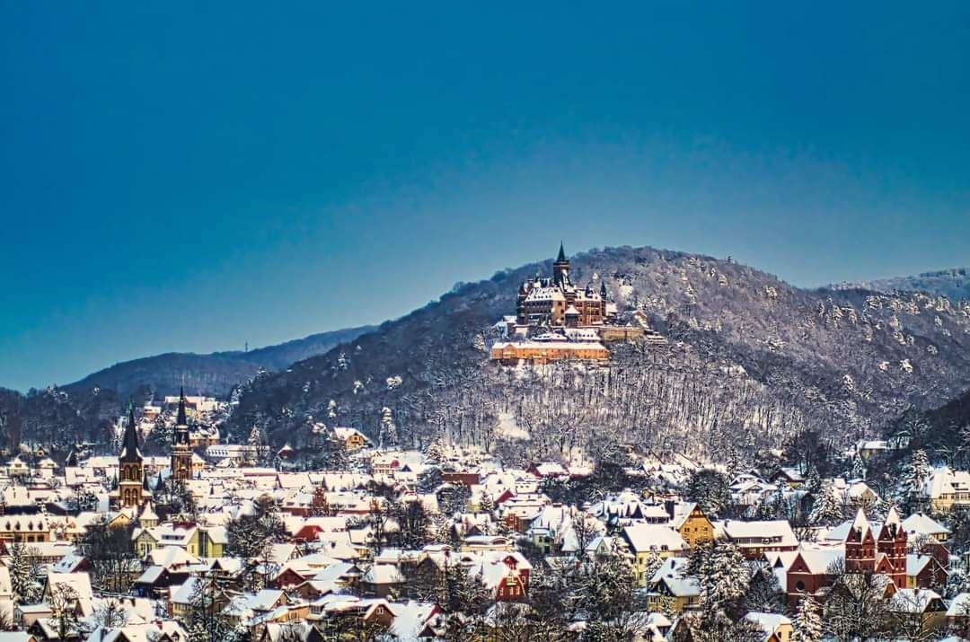 Schloss auf Berg mit schneebedecktem Dorf im Vordergrund.