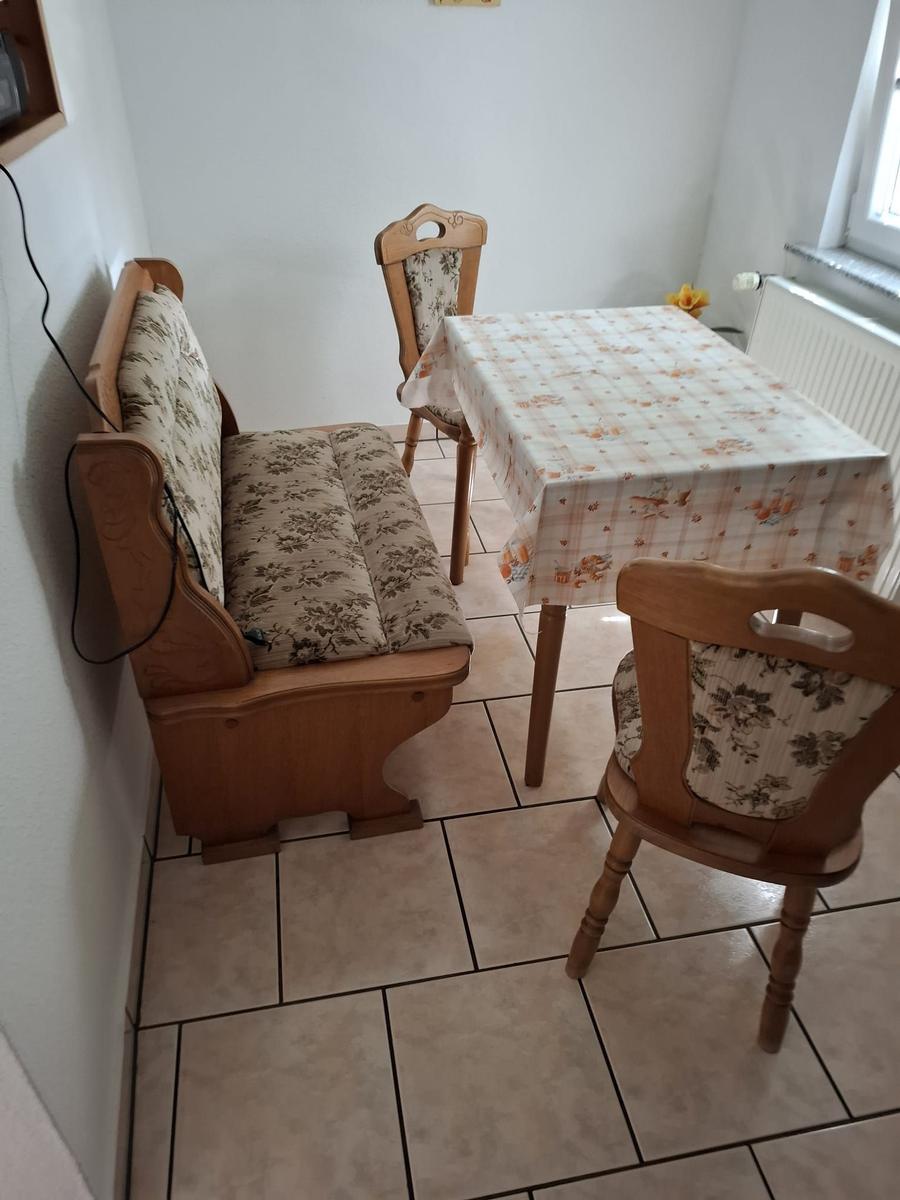 Essbereich mit Tisch, drei Stühlen und Sitzbank. Bodenfliesen und Fenster vorhanden.