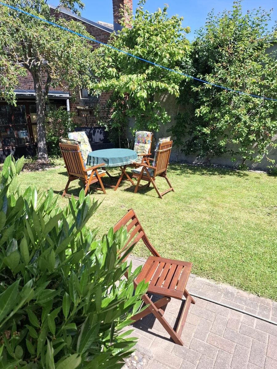 Hinterhof mit Garten, Tisch und Stühlen. Grünfläche, Bäume und Pflanzen.