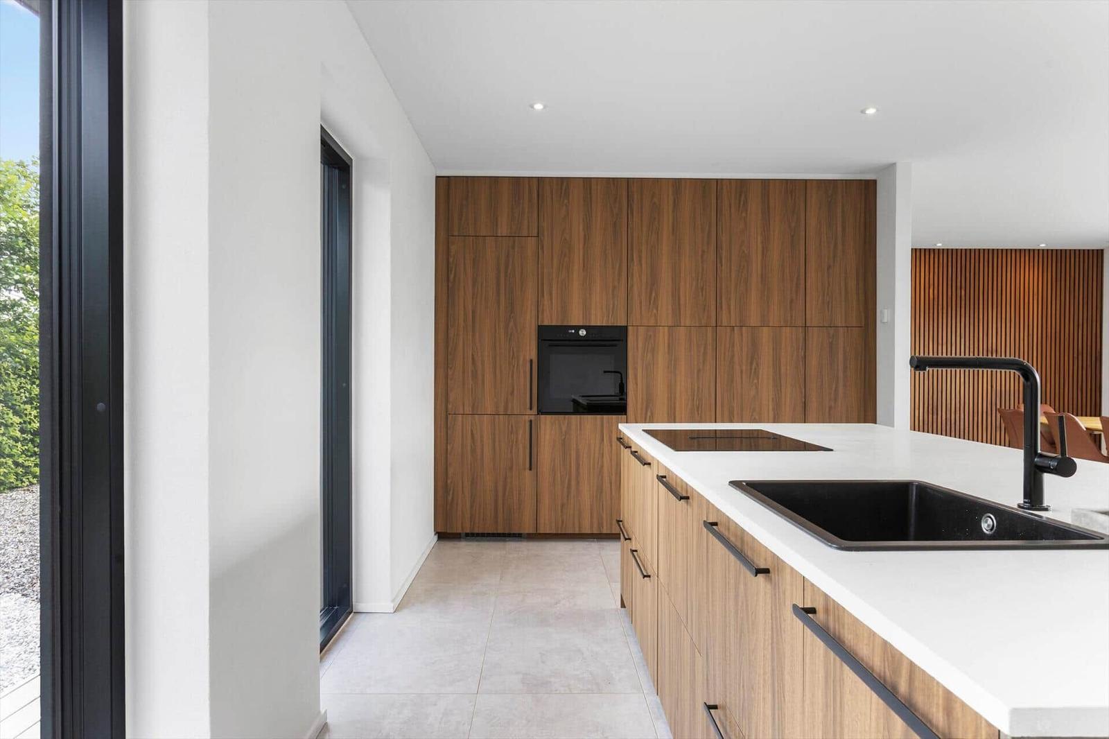 Moderne Küche mit Holzschränken, Edelstahlspüle und integriertem Ofen.