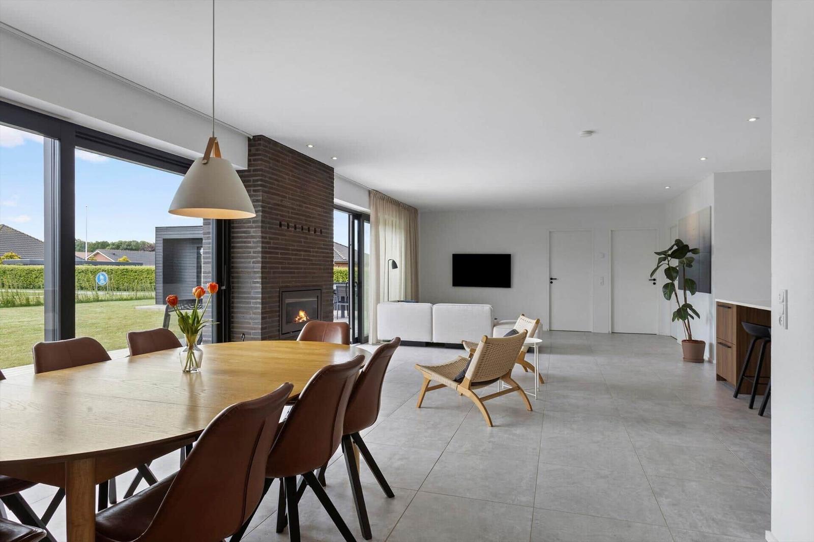 Großes Wohn- und Esszimmer mit Holztisch, Sitzgelegenheiten und Kamin. Blick auf grünen Garten.