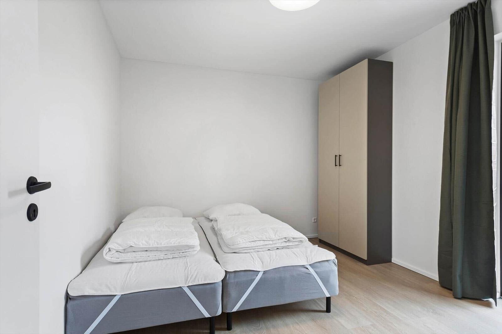 Zimmer mit zwei Einzelbetten, Kleiderschrank und Fenster mit Vorhang.
