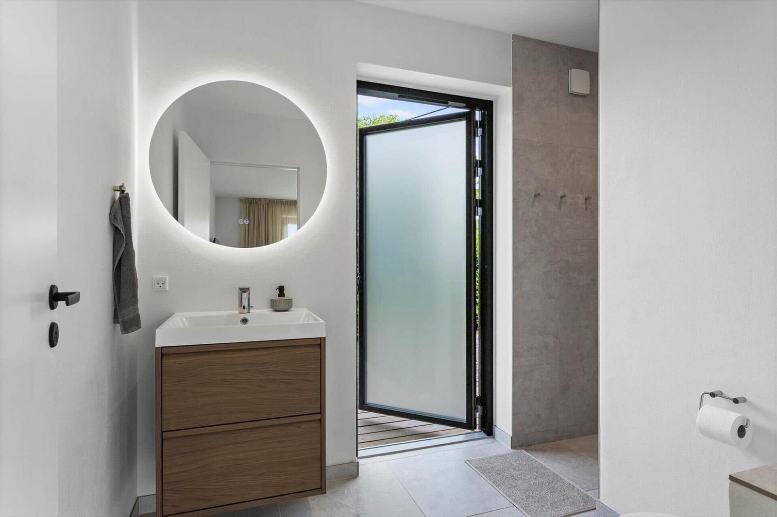 Badezimmer mit Waschbecken, Spiegel und Tür zur Terrasse.