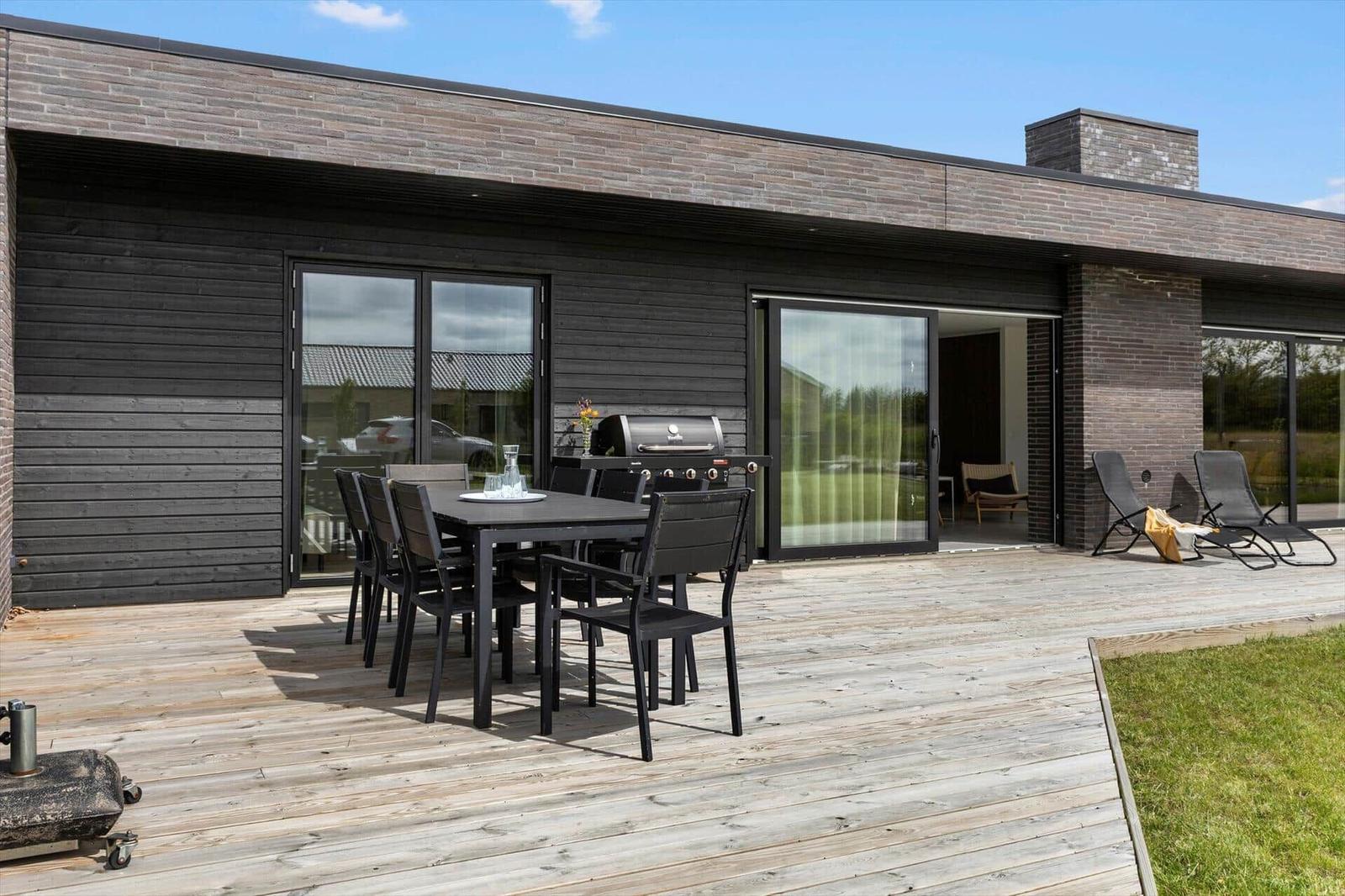 Terrasse mit Tisch, Stühlen und Grill. Durchgehende Glasfront zum Innenraum.