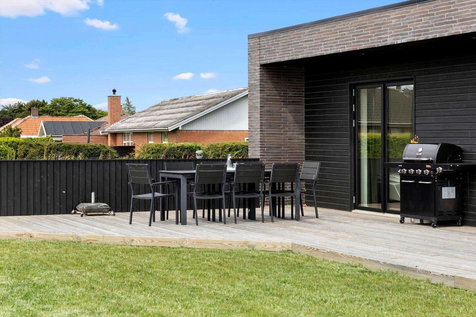 Terrasse mit Tisch, Stühlen und Grill neben modernem Haus mit Holz- und Ziegelsteinfassade.