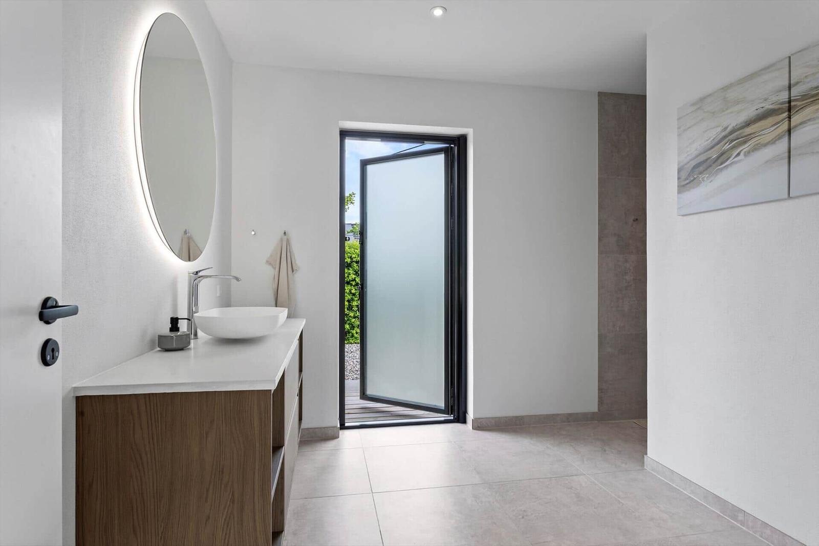Badezimmer mit Waschbecken, Spiegel und Glastür zur Terrasse.
