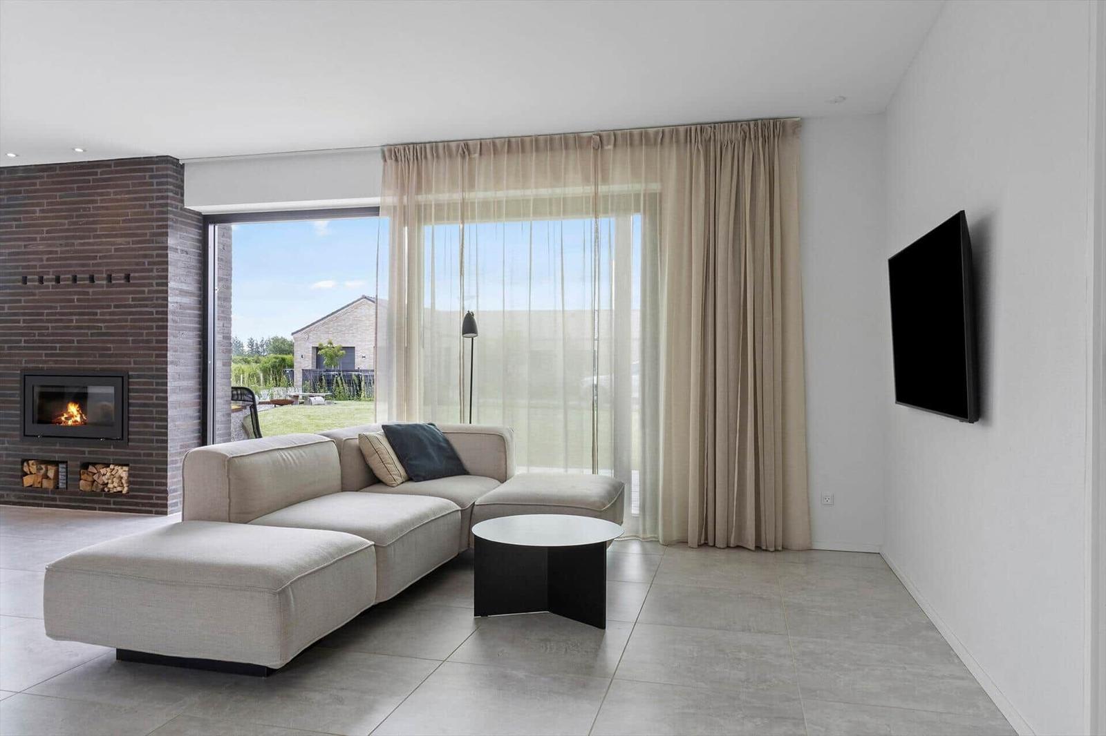 Wohnzimmer mit Sofa, Kamin und großem Fenster zur Außenterrasse.