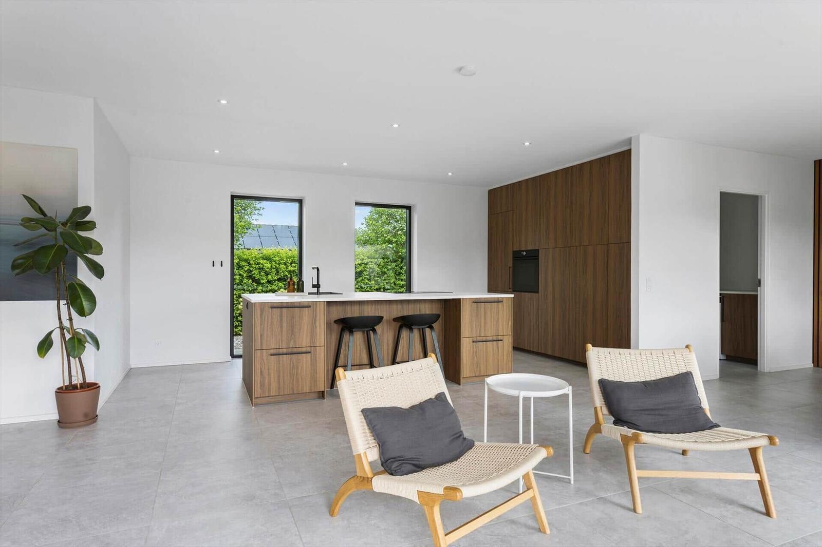 Küche mit Holzschränken und Sitzgelegenheiten. Große Fenster und Pflanze sichtbar.