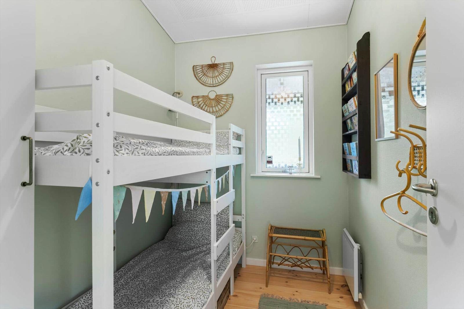 A bedroom with a white bunk bed, a window, and a bookshelf on the wall.