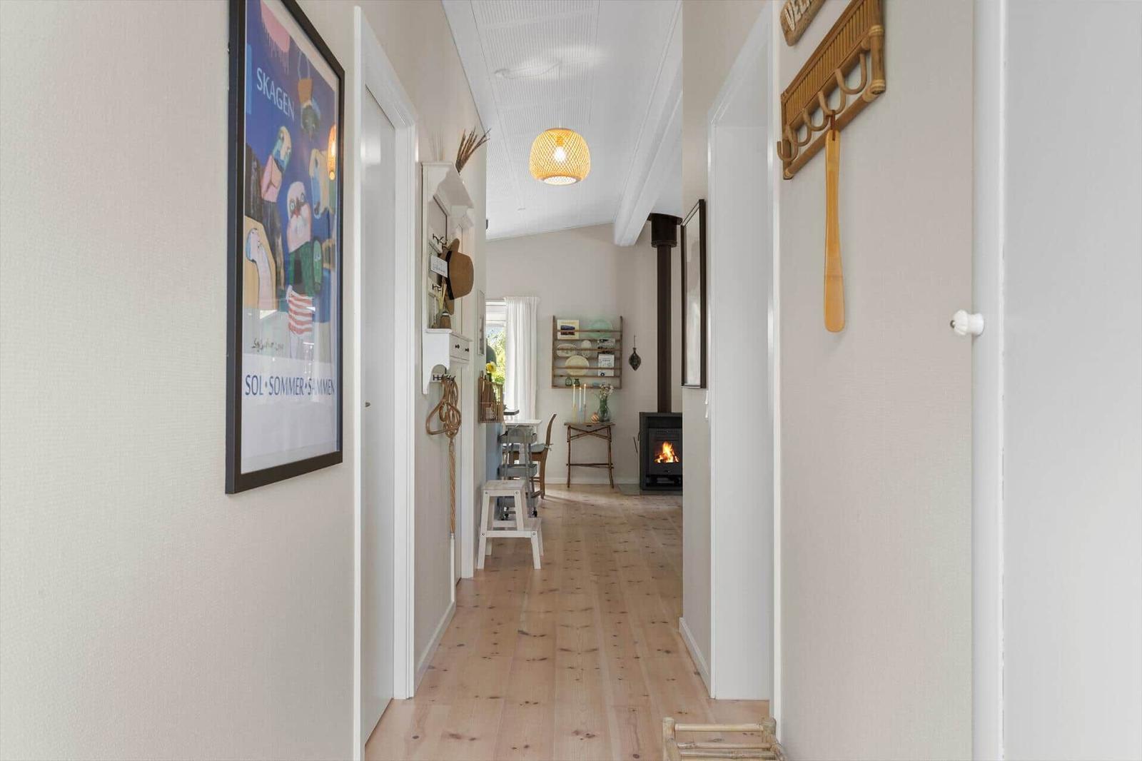 Hallway with wooden floor, wall art, and fireplace in the background.