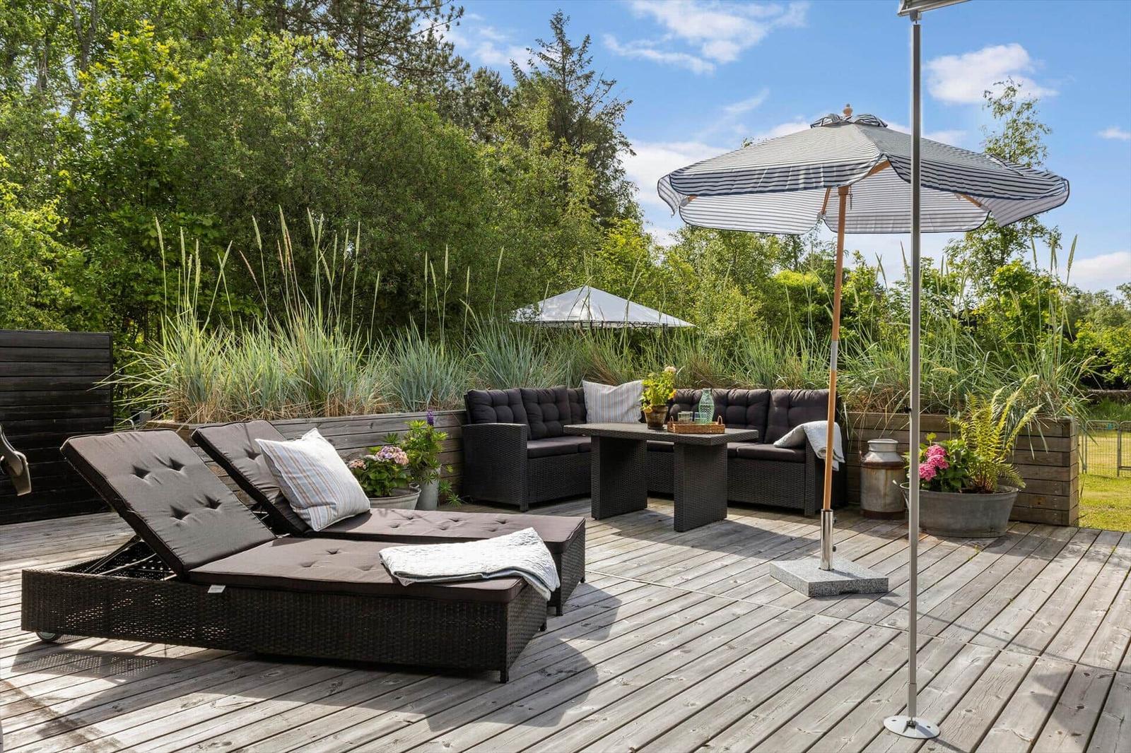 Deck with loungers, seating group, and umbrella. Surrounded by greenery and plants.