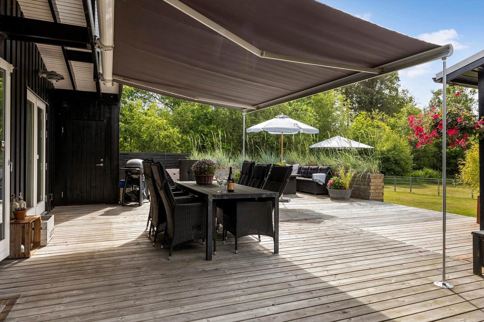 Deck with seating, grill, and awning. Background with greenery and flowers.