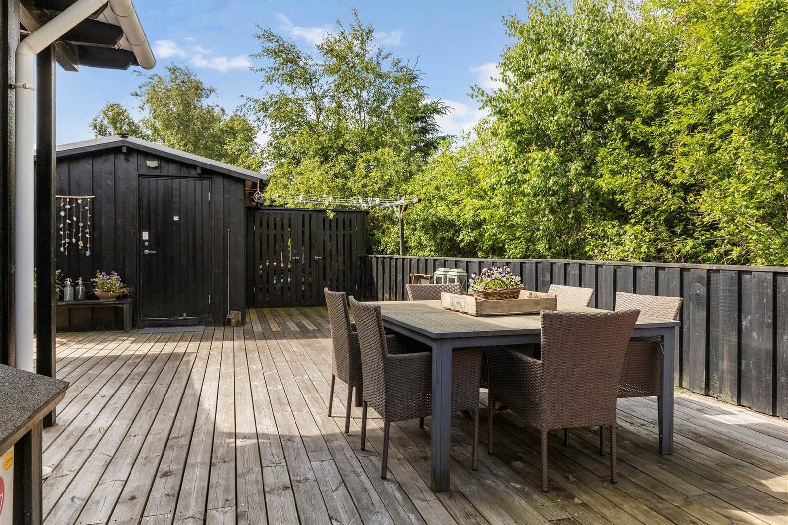 Deck with table and chairs, surrounded by trees and a wooden shed.