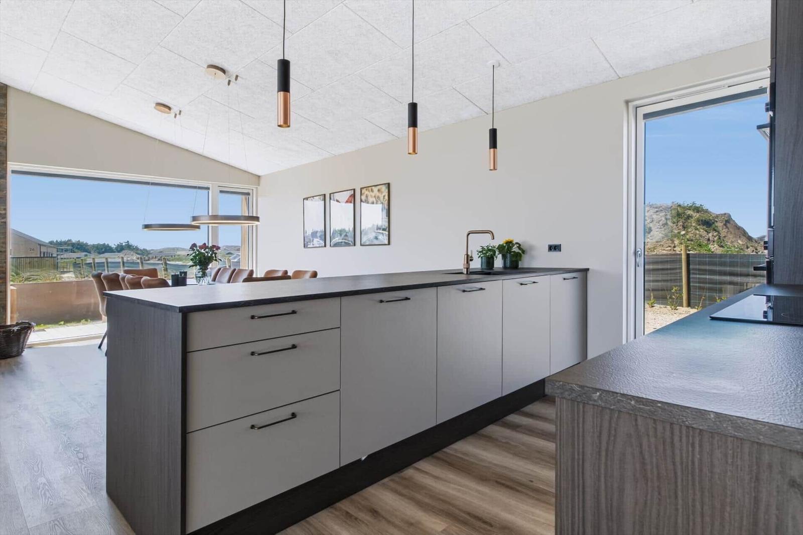 Moderne Küche mit Kücheninsel, schwarzer Arbeitsplatte und großem Fenster mit Blick auf Landschaft.