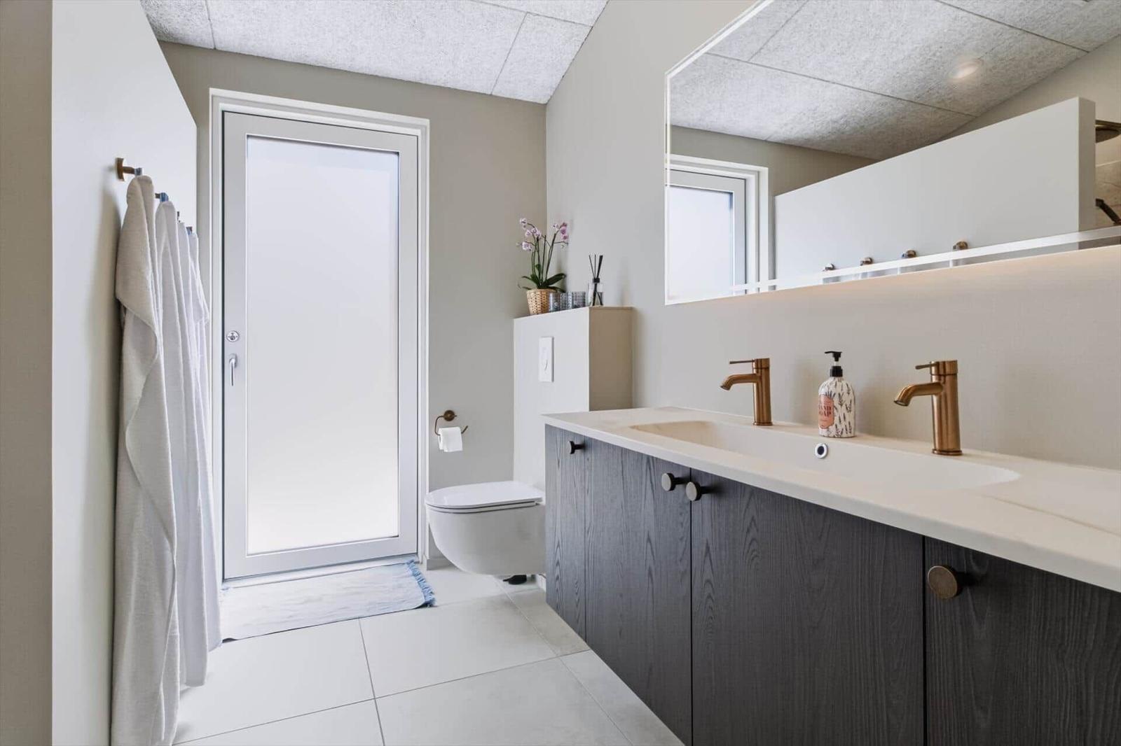Badezimmer mit Doppelwaschbecken, Spiegel und Toilette. Tür führt nach draußen.