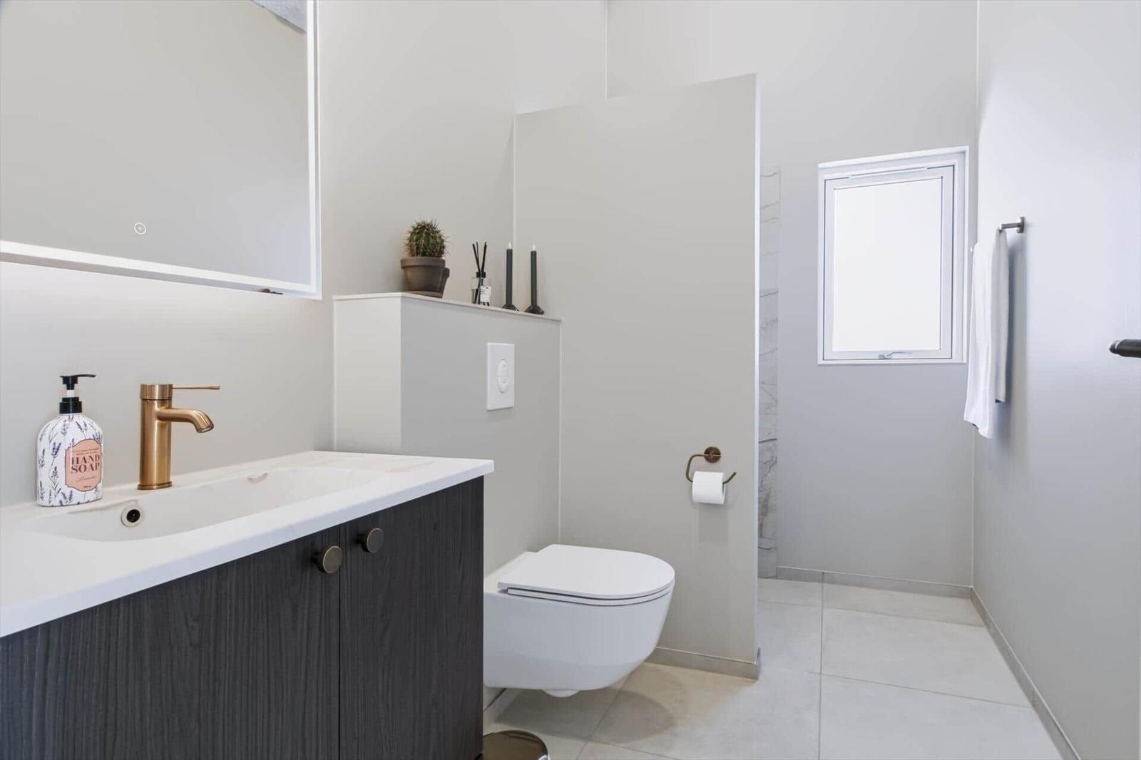 Bad mit Waschbecken, Toilette und Dusche. Goldfarbener Wasserhahn und Spiegelschrank.
