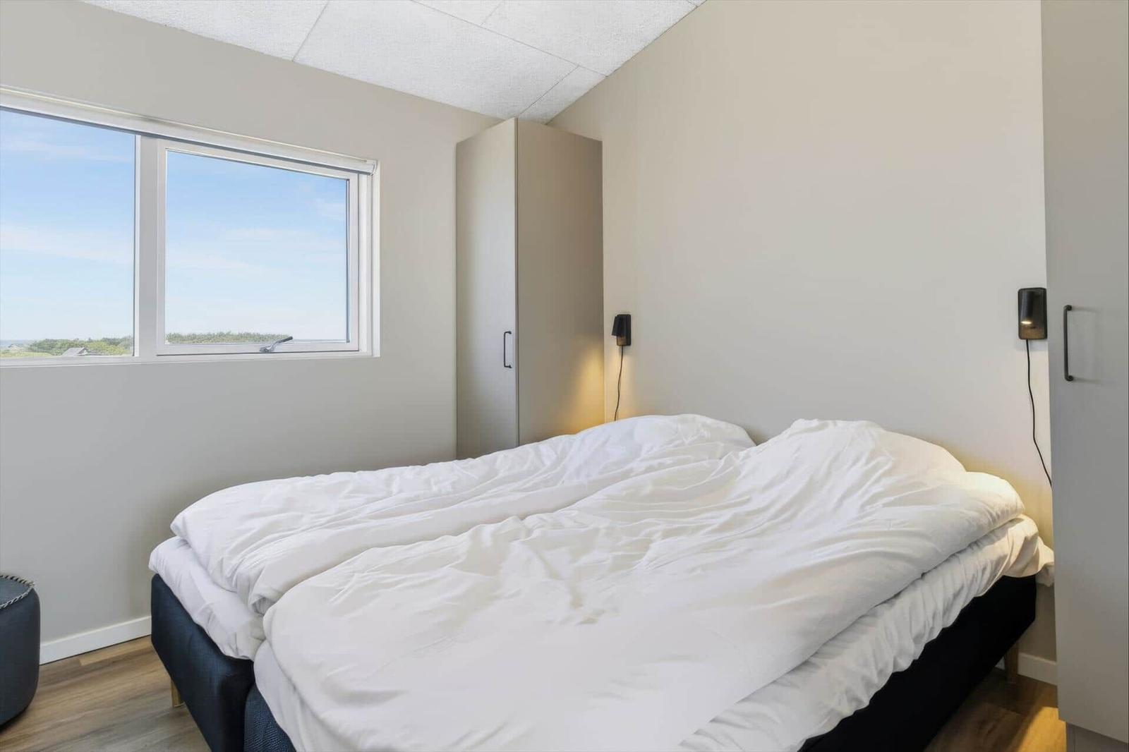 Schlafzimmer mit Doppelbett, Fenster und Kleiderschrank.