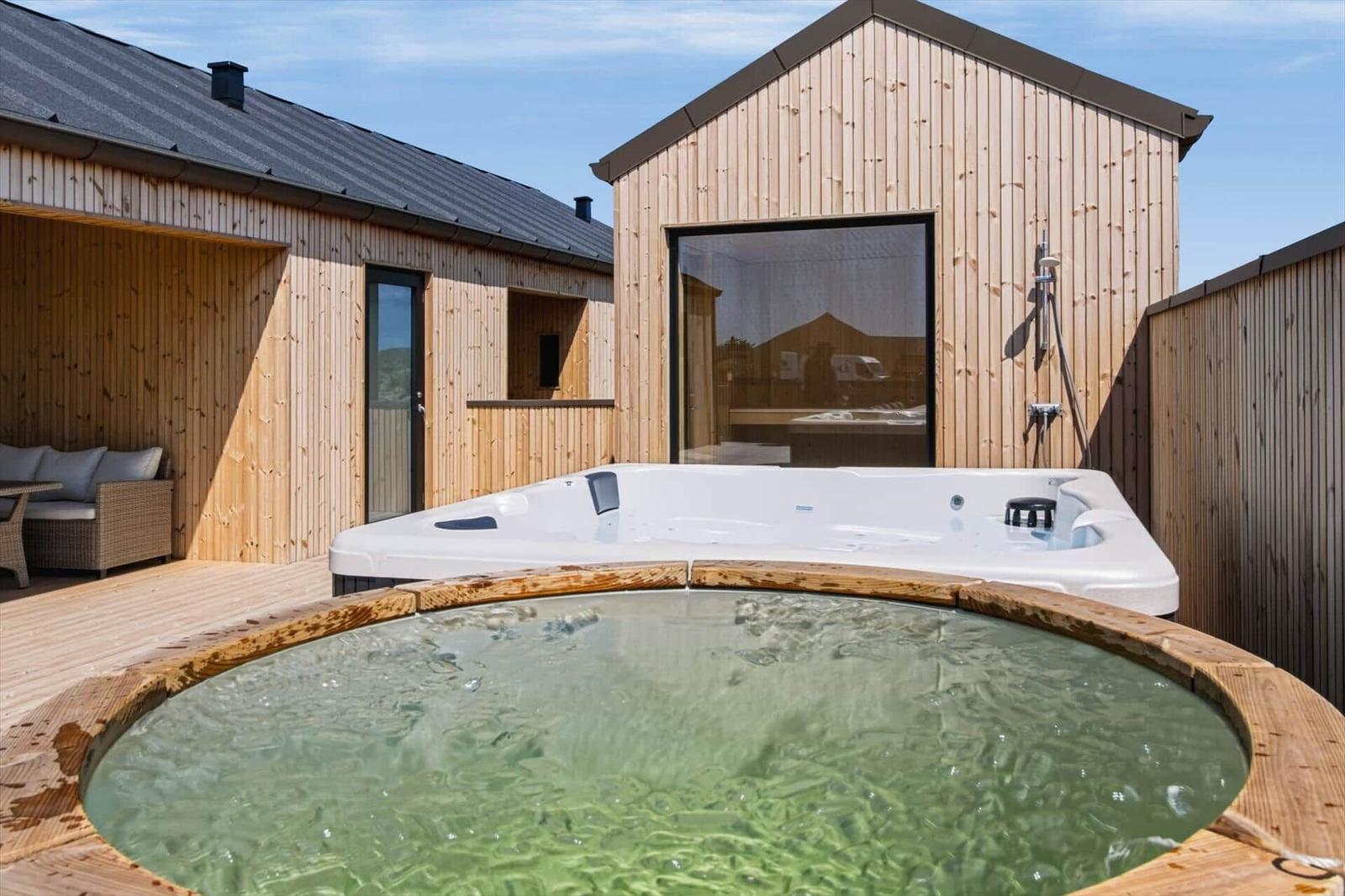 Außenbereich mit Whirlpool und Holzterrasse. Hintergrund: Holzhaus mit Glasfront.