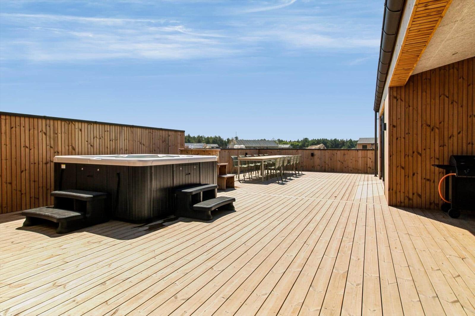 Terrasse mit Whirlpool, Tisch und Stühlen. Holzdecke und Holzwand. Blick auf Wald und Himmel.