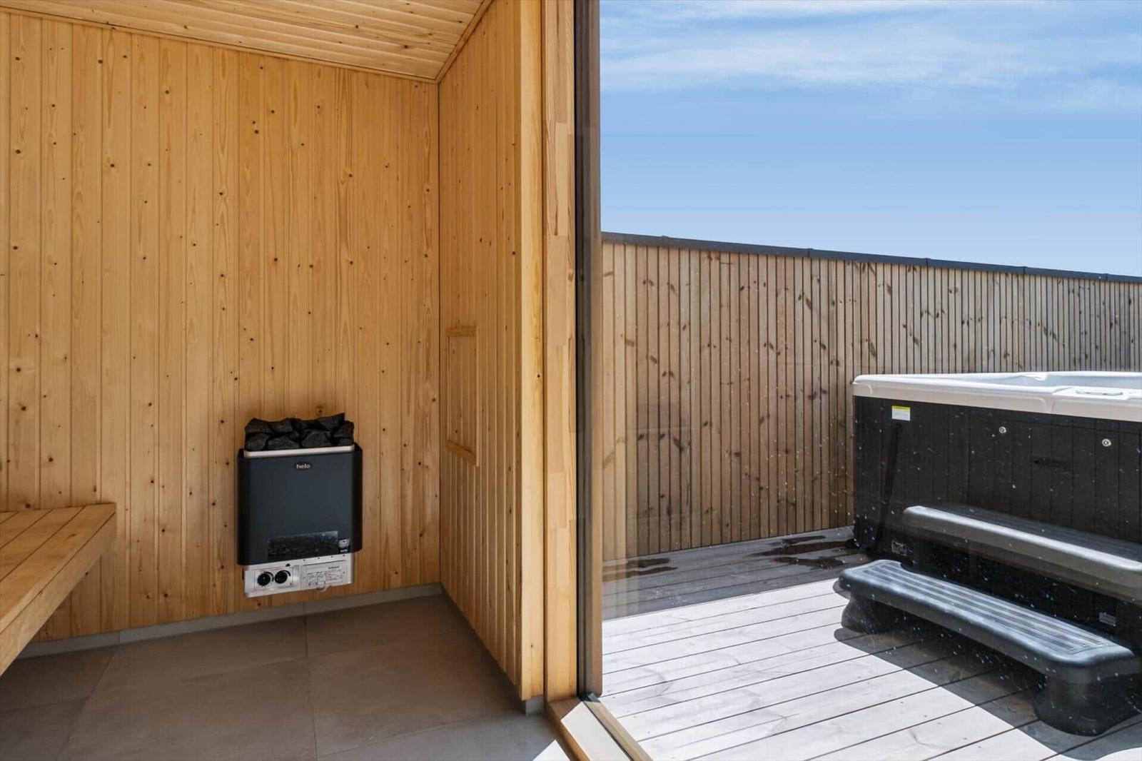 Sauna mit Holzwand und Heizgerät, Blick auf Terrasse mit Whirlpool und Holzgeländer.