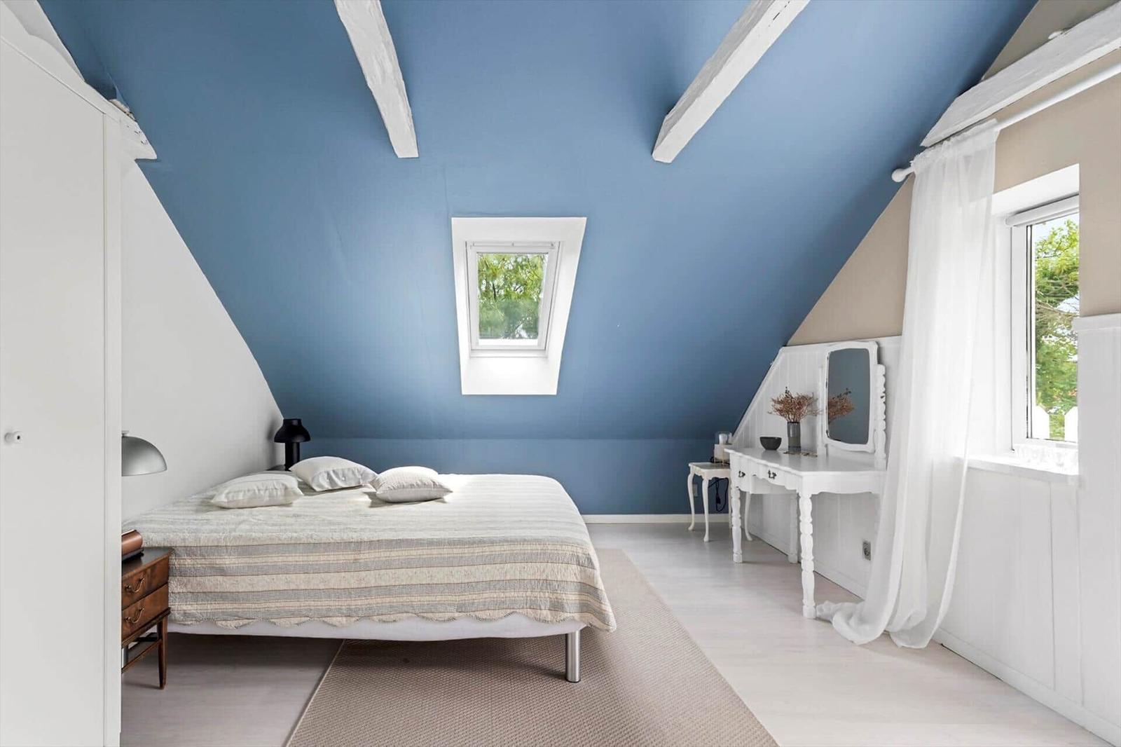 Schlafzimmer mit blauem Dach, weißem Schrank, Bett und Schreibtisch.