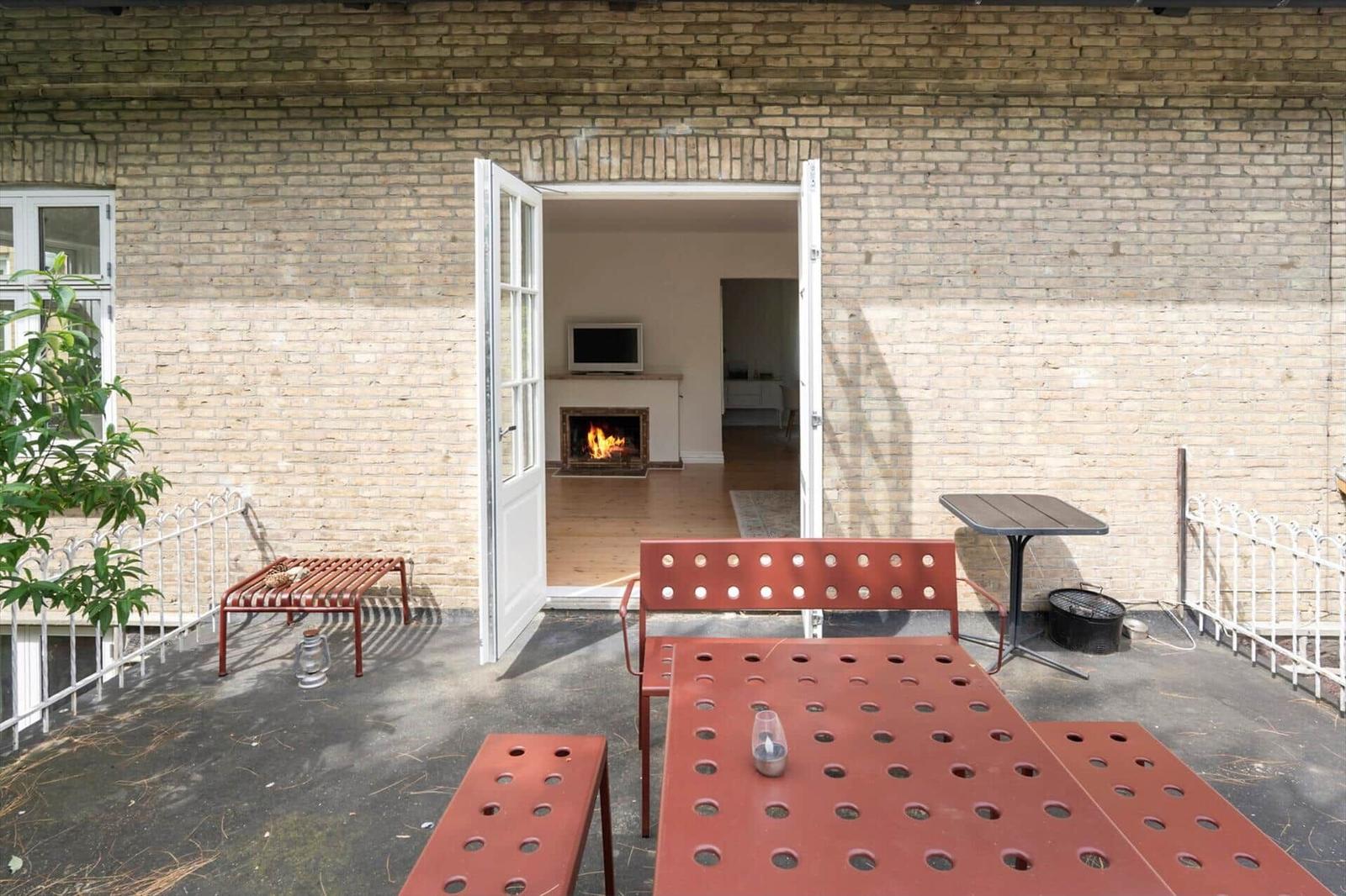 Terrasse mit rotem Metallmöbel und offenem Durchgang zum Innenraum mit Kamin.