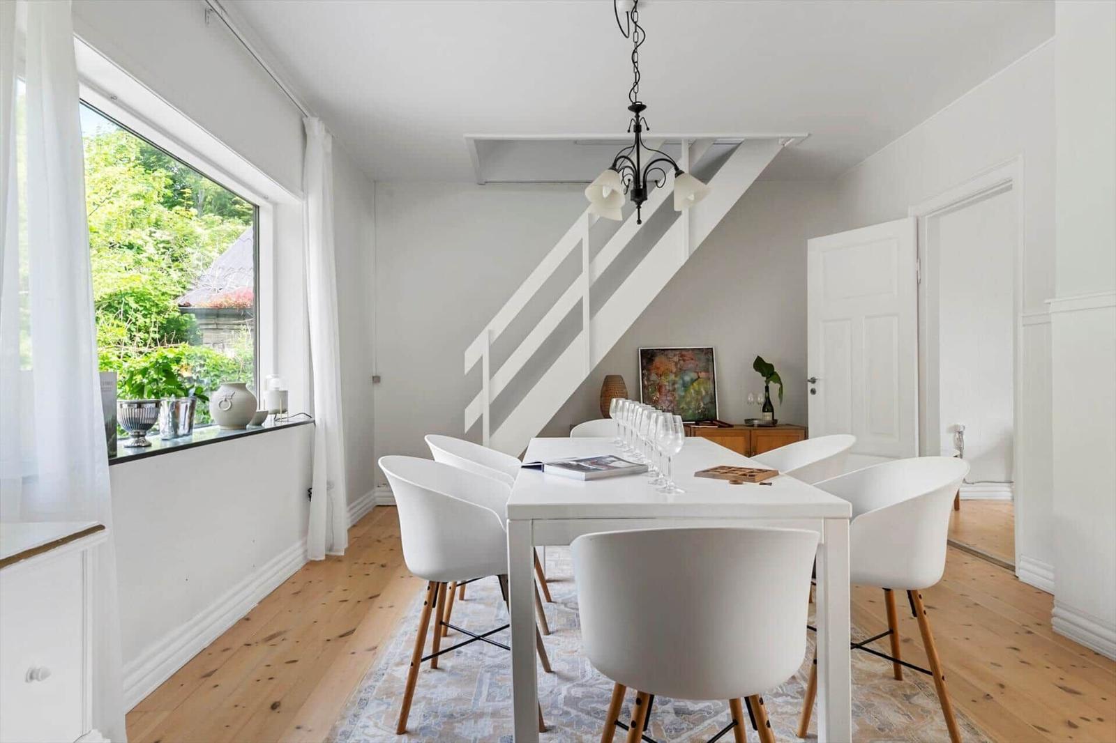 Esszimmer mit weißem Tisch, Stühlen und Fensterblick auf Garten