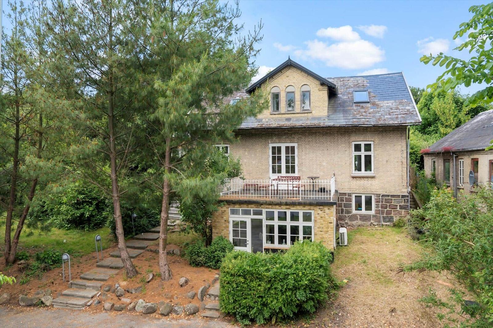 Ein zweistöckiges Haus mit Balkon und Garten. Umgeben von Bäumen und Sträuchern.