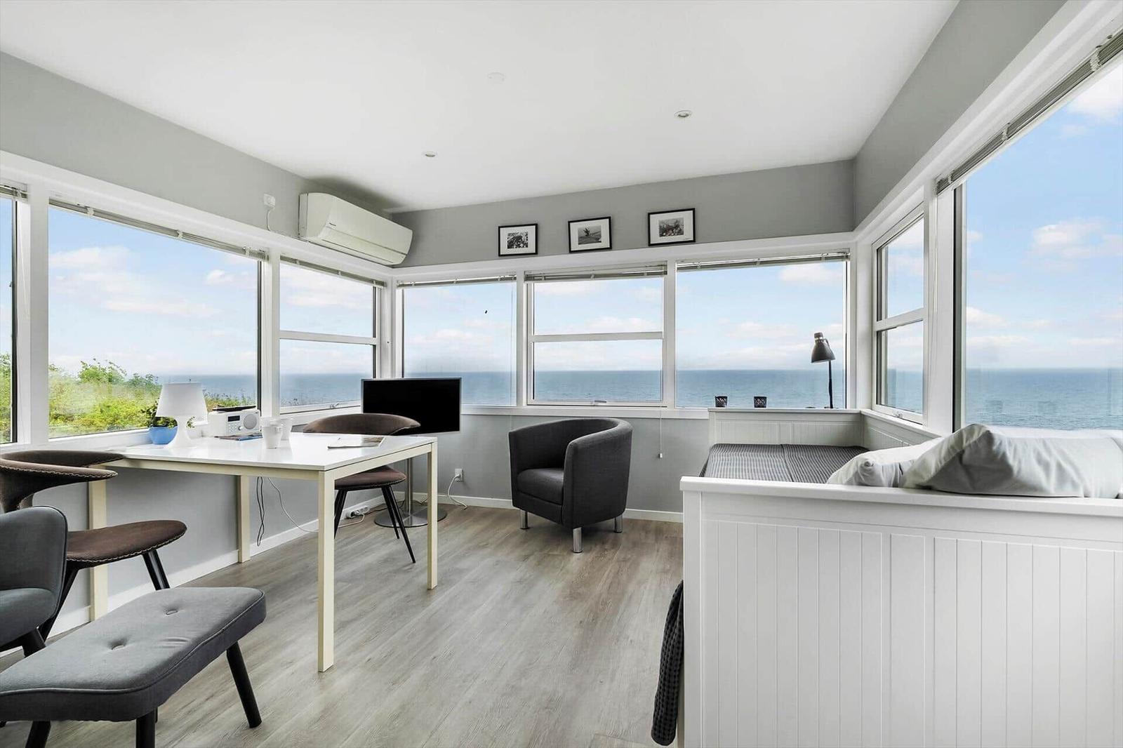 Raum mit großem Fensterblick aufs Meer, Schreibtisch, Sessel und Schlafcouch.