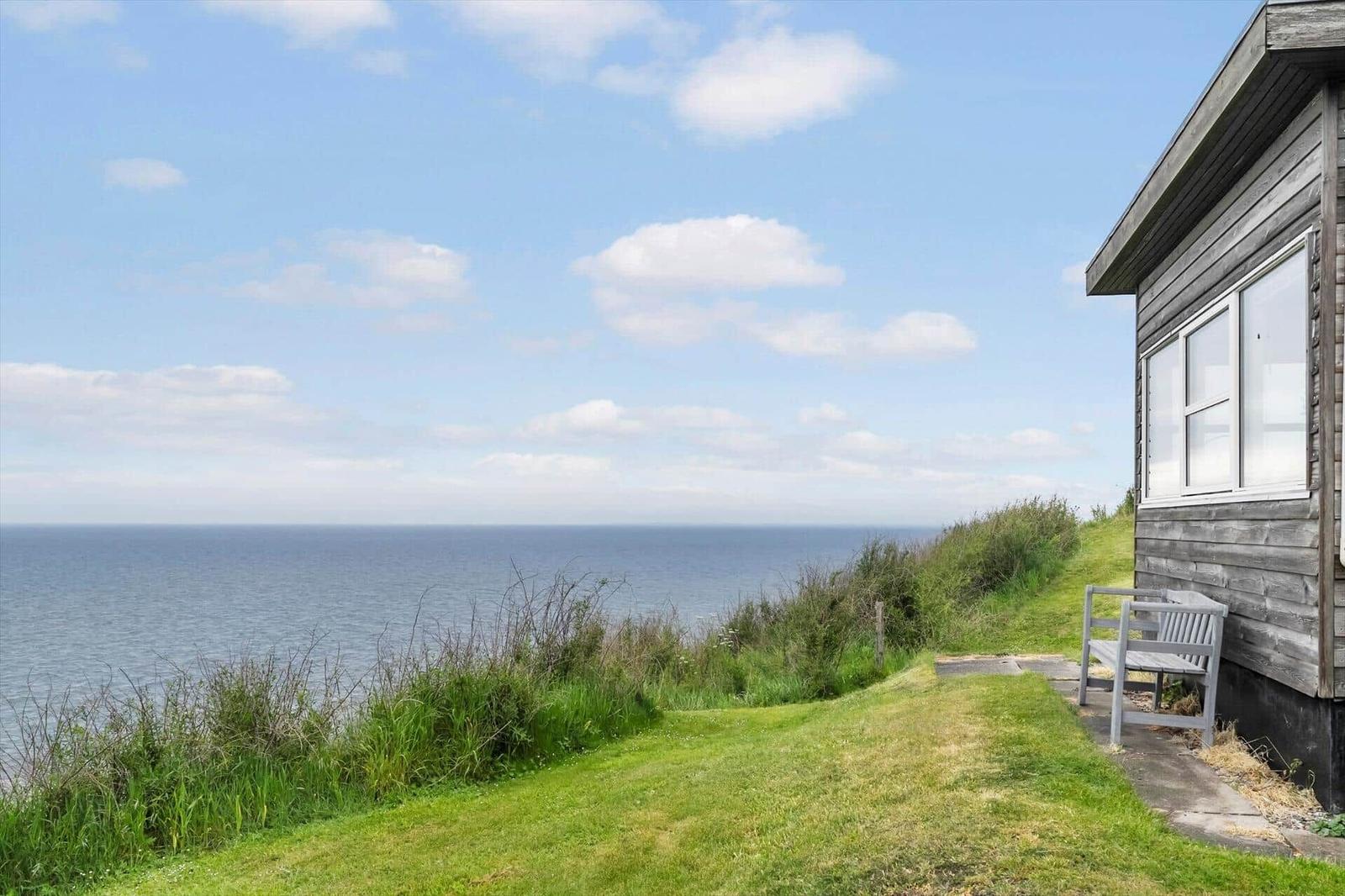 Haus mit Blick auf das Meer, grüner Rasen und Bank vor der Wand.
