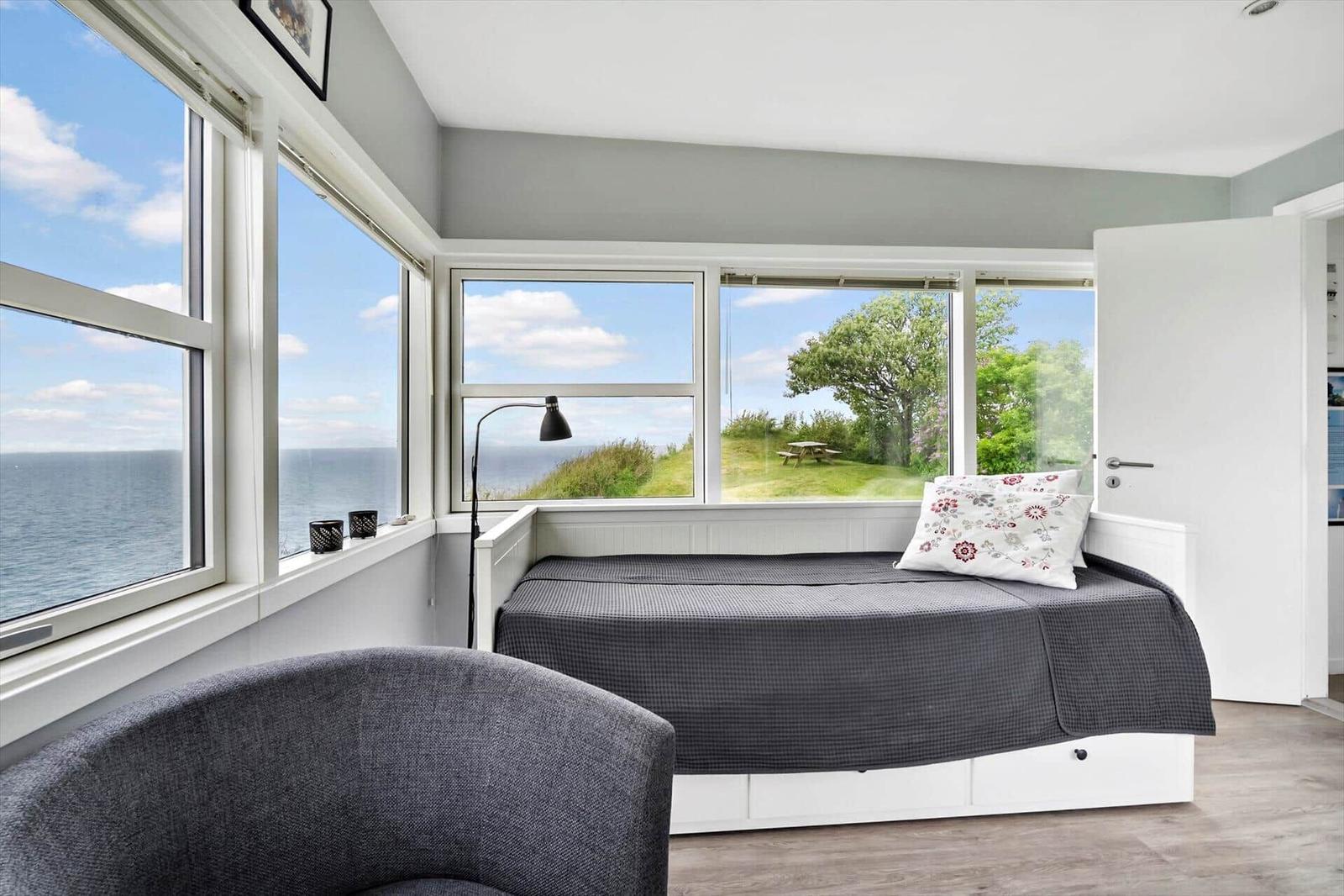 Schlafzimmer mit Blick auf Meer und Grünfläche. Bett, Sessel und Fenster sind sichtbar.