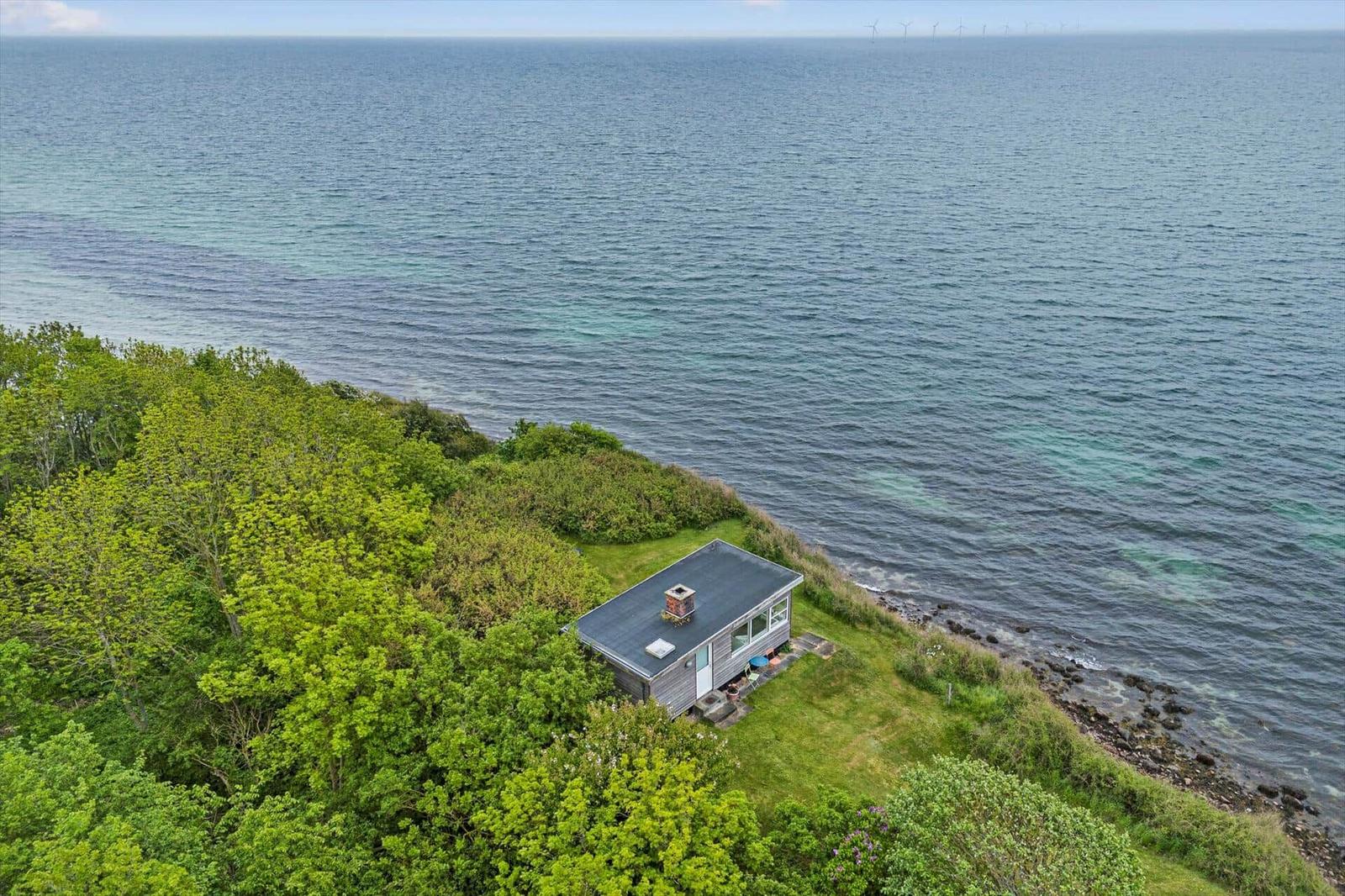 Kleines Haus auf einer grünen Halbinsel direkt am Meer mit Blick auf Windkraftanlagen.