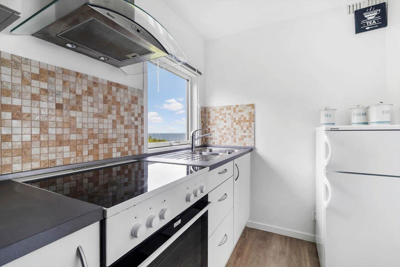 Küche mit Dunstabzug, Herd und Küchenzeile. Fenster mit Meerblick. Kühlschrank und Aufbewahrung.