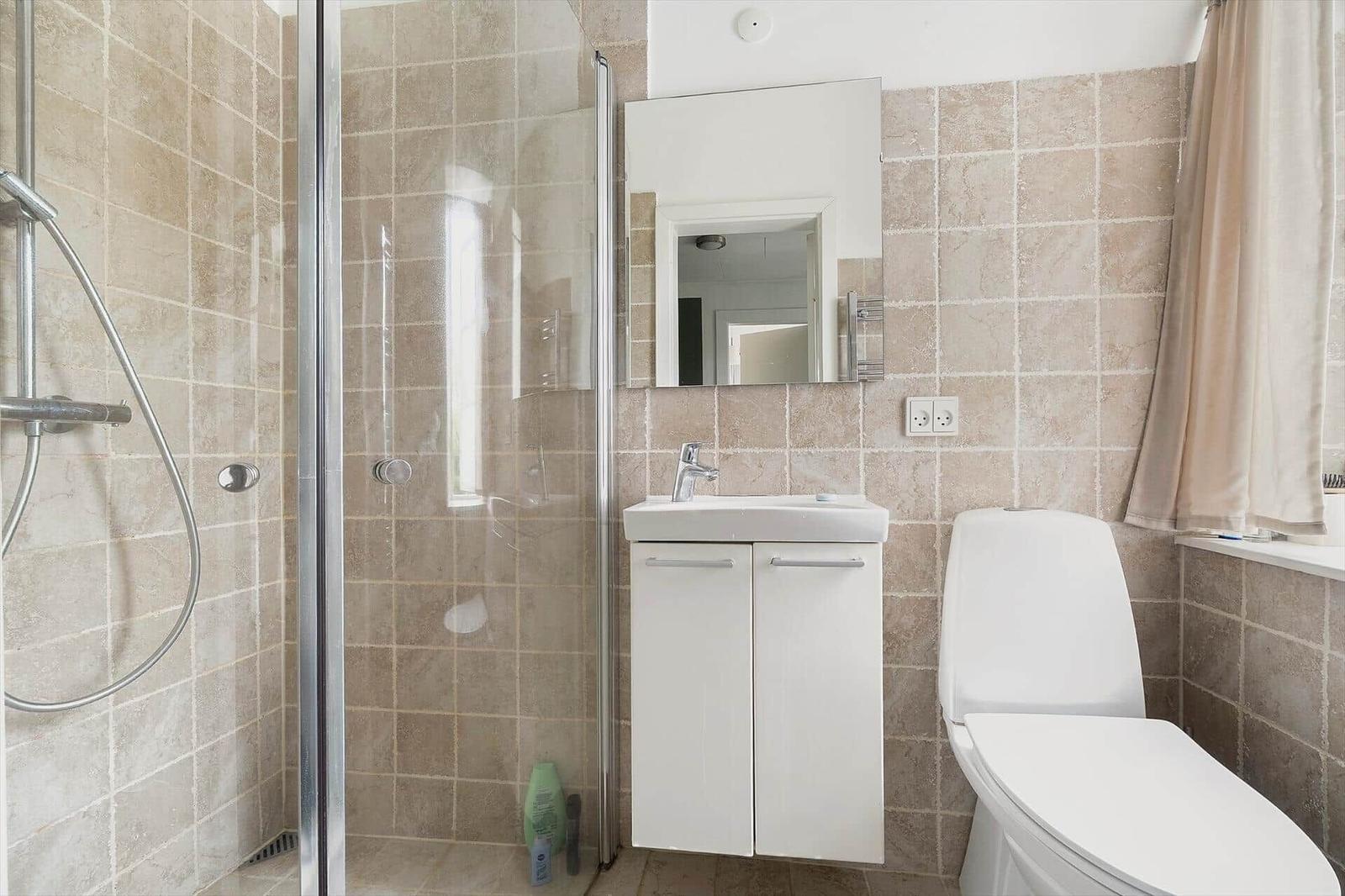 Badezimmer mit Dusche, Waschbecken und Toilette. Fliesenwand und Spiegelschrank.