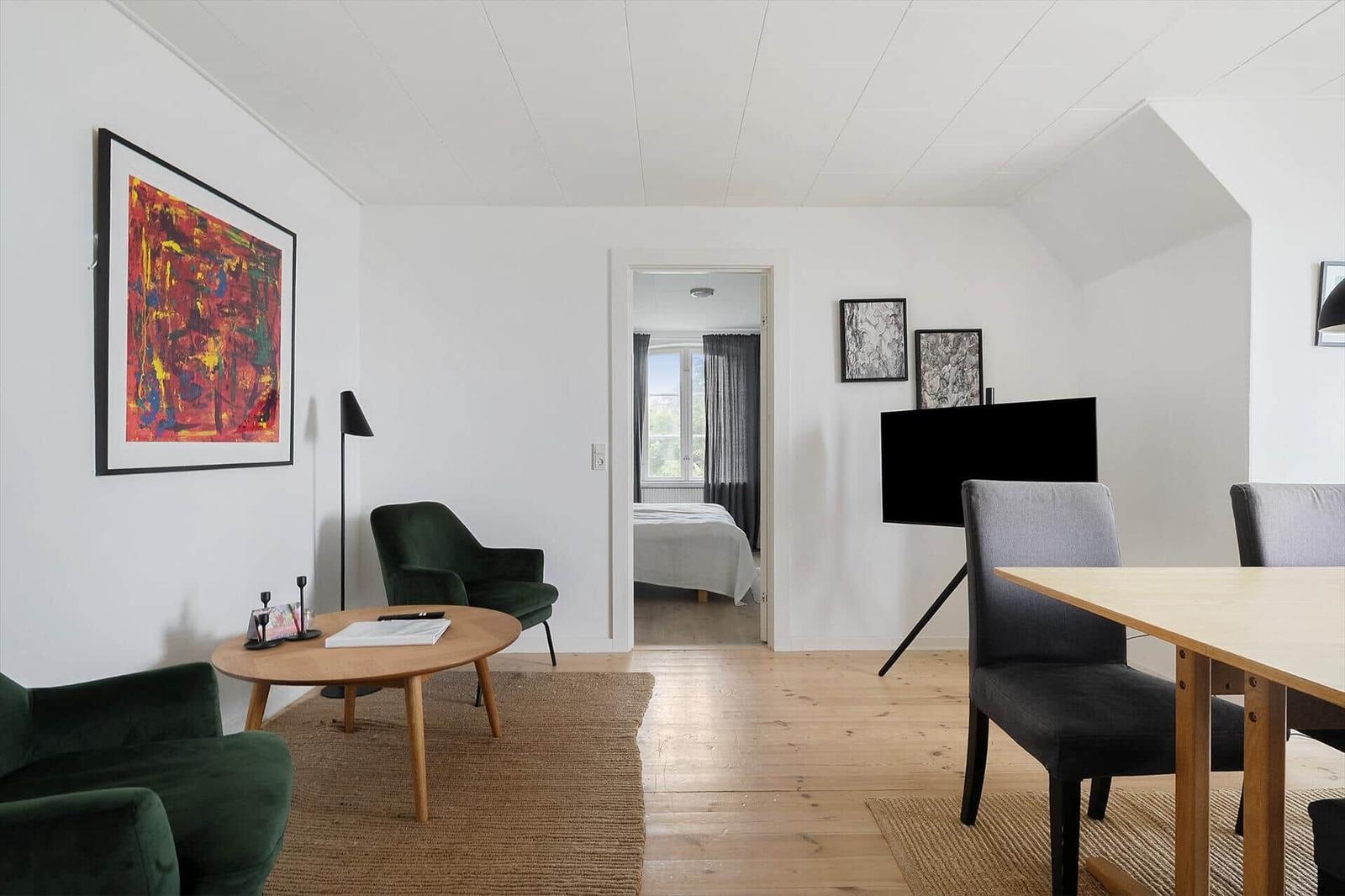 Wohn- und Essbereich mit grünen Sesseln, Holztisch und Fernseher. Durchgang zur Schlafzimmer.