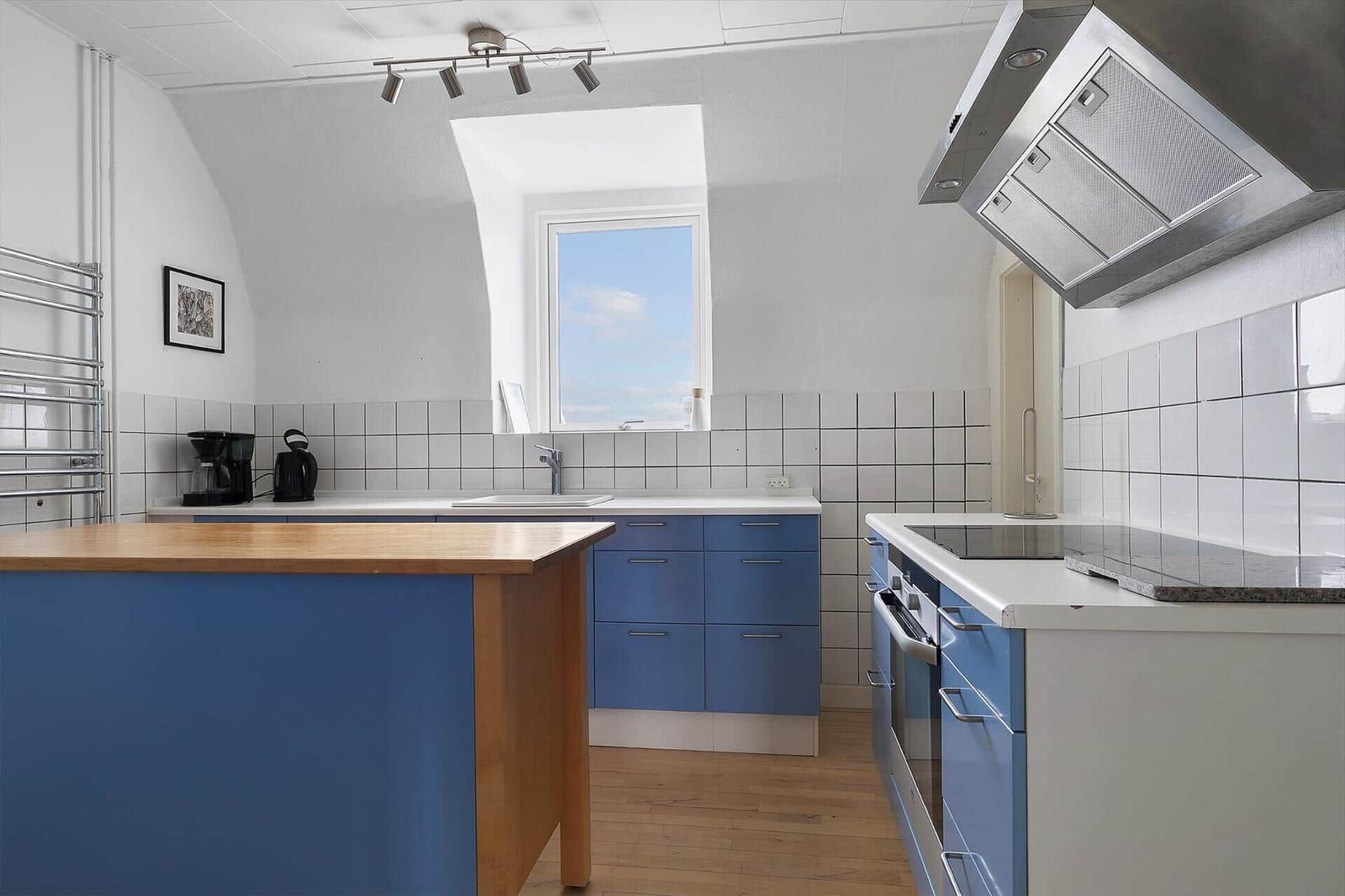 Küche mit blauen Schränken, Holzoberfläche und Fenster mit Blick auf den Himmel.