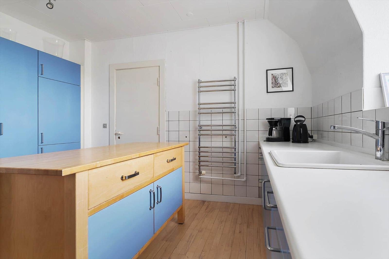 Küche mit blauen Schränken, Holzoberfläche und weißen Fliesen an der Wand.