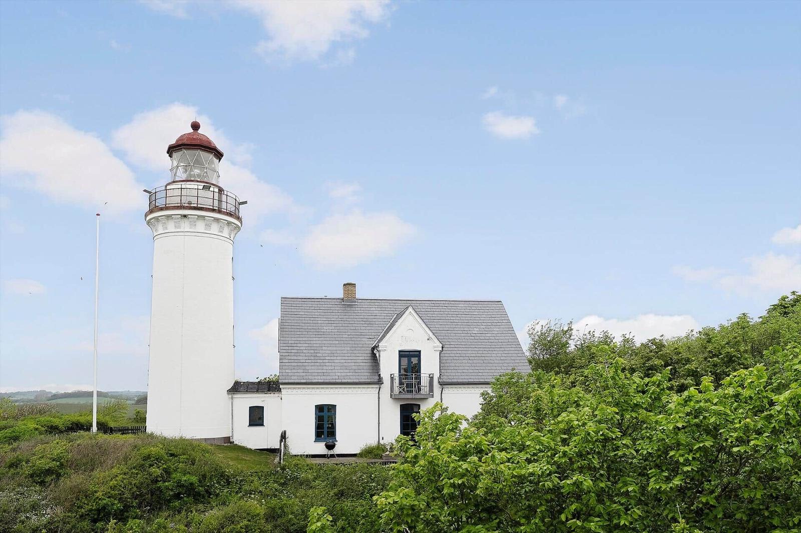 Weißer Leuchtturm mit Anbauhaus auf grüner Fläche unter blauem Himmel.