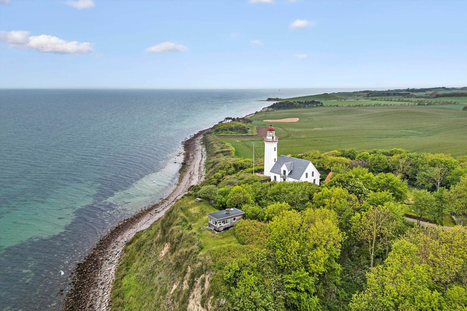 Weißer Leuchtturm und Haus auf grüner Halbinsel mit Meeresblick.
